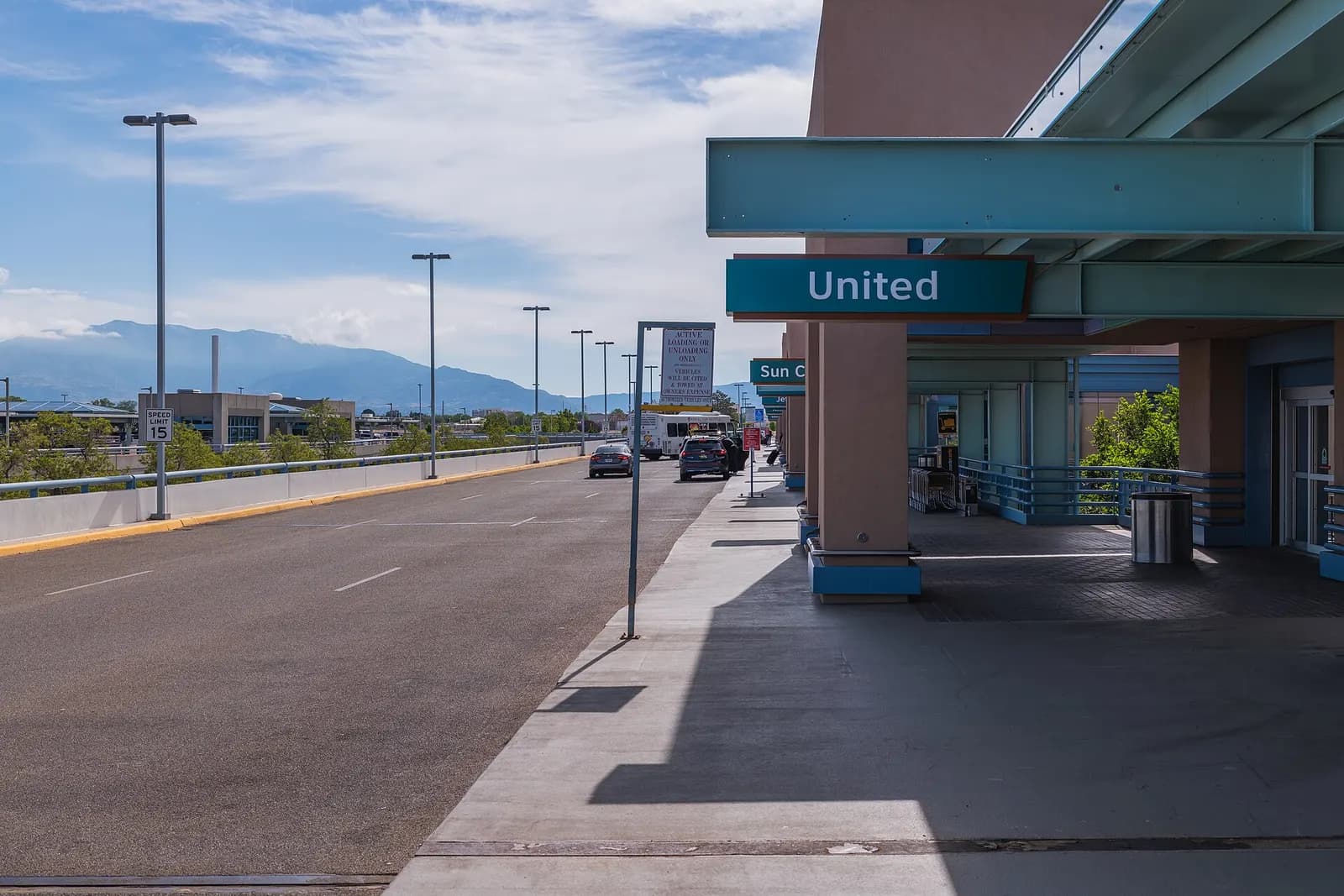 Departures curbside at Albuquerque International Sunport in May 2026, with airline signs over the entrance and the Sandia Mountains behind the terminal.