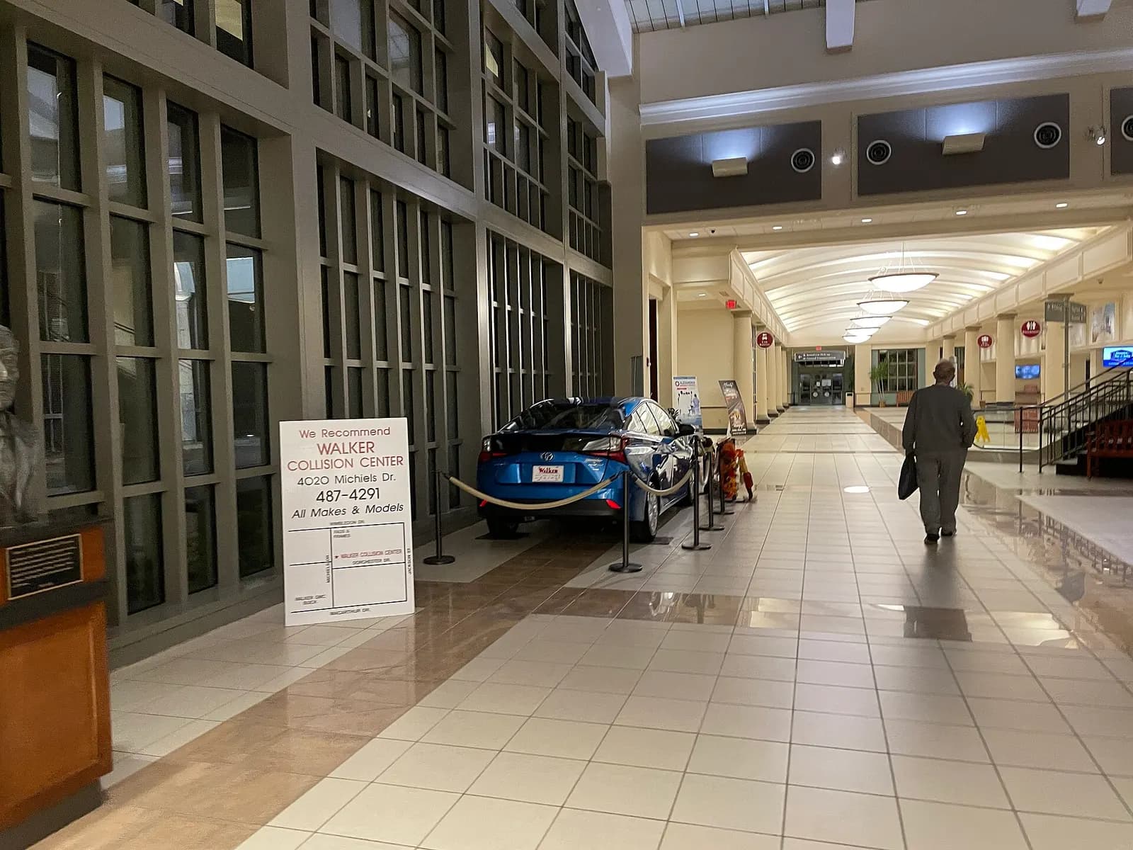 Long tiled landside hall at Alexandria International Airport with a leftover display sedan and a leftover Walker Collision Center sign.