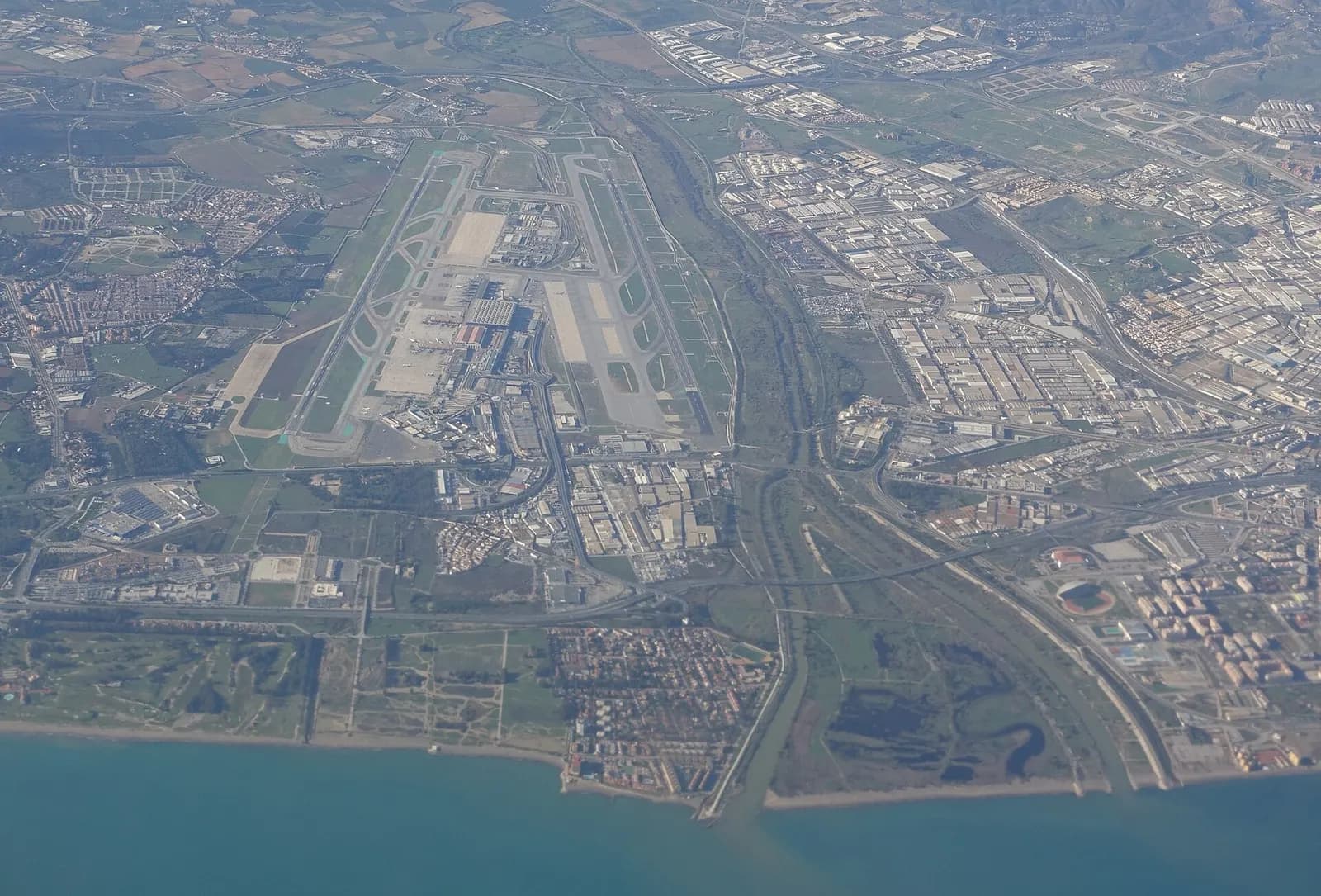 From a departing aircraft, Málaga-Costa del Sol Airport's runways, terminals, and coastal surroundings spread out below toward the Mediterranean.