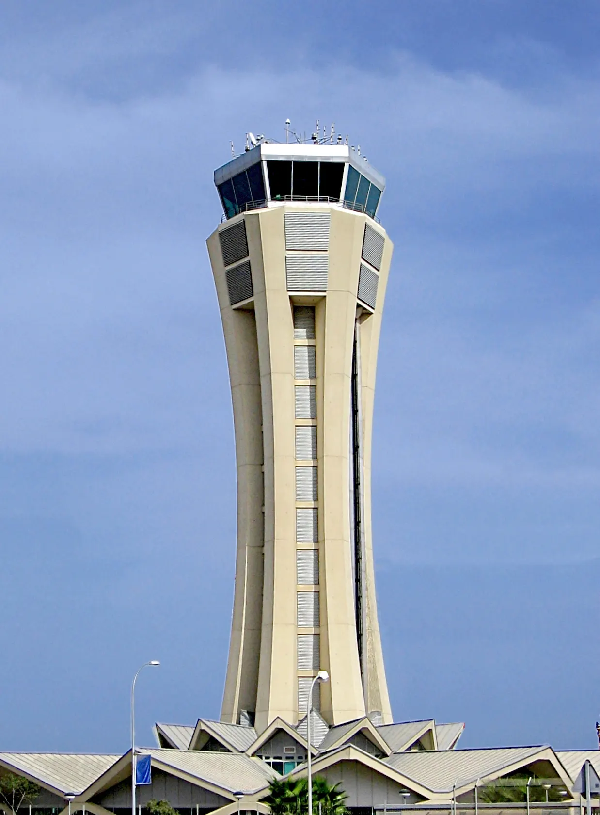 The tall air-traffic control tower at Málaga Airport rises above the terminal rooftops against a clear sky.