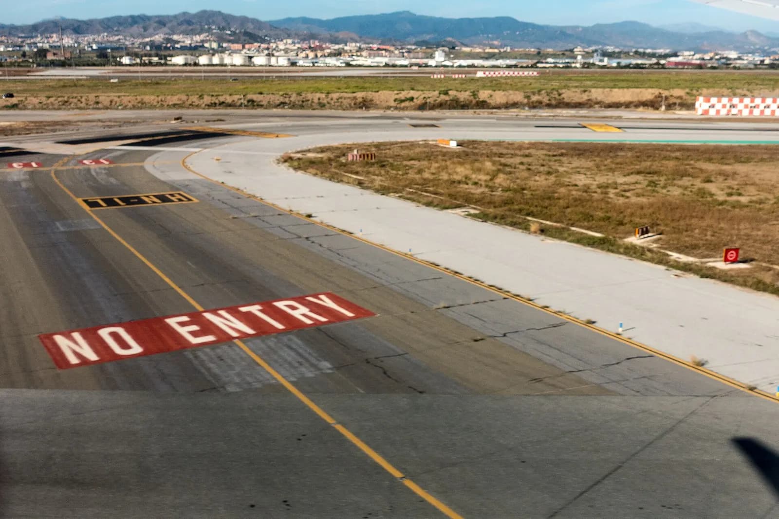 The modern glass-and-steel terminal complex of Málaga-Costa del Sol Airport stretches across the frame under a bright sky, with roads and landscaping in the foreground.