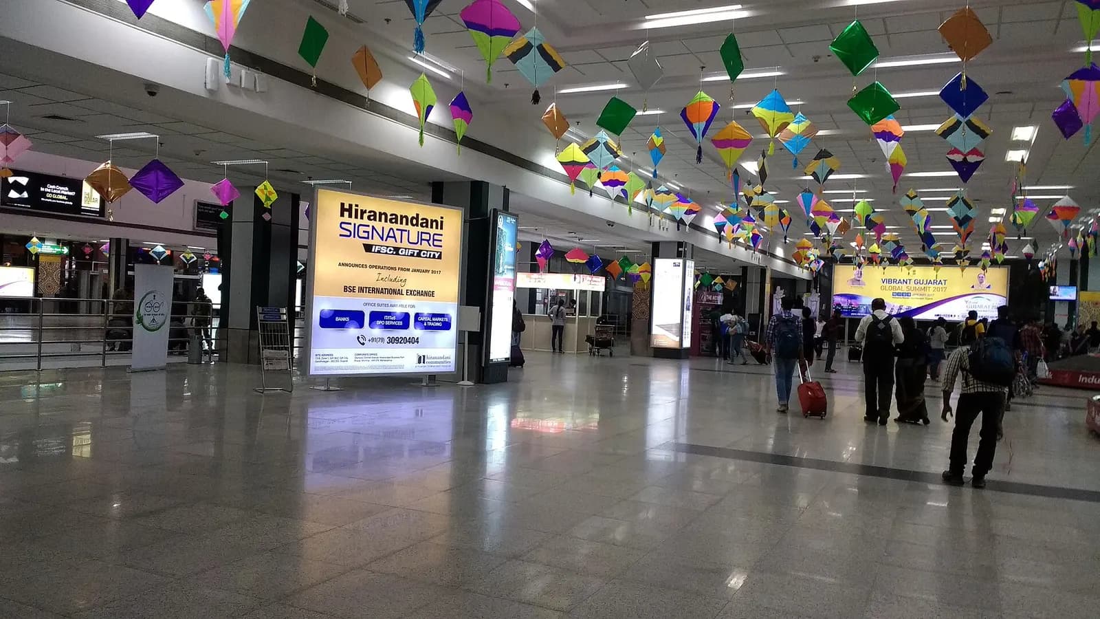 Interior hall at Ahmedabad airport with hanging kite decorations and traveler traffic