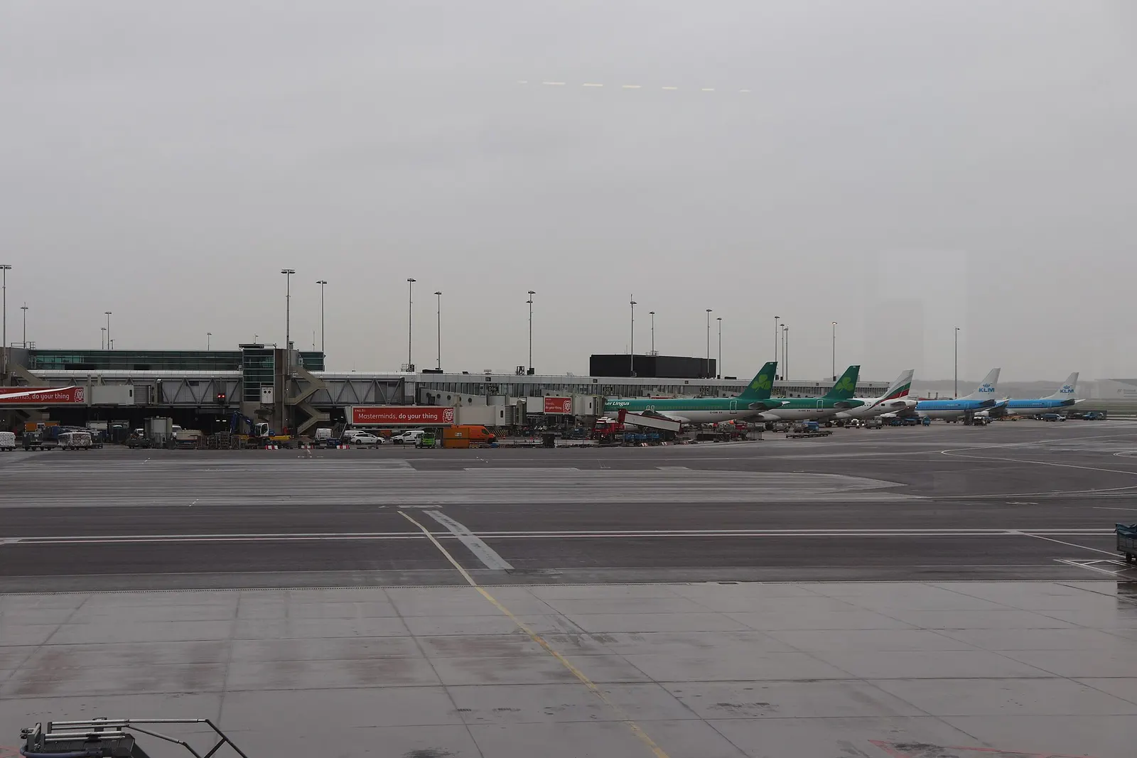 The long gate corridor of Pier D at Schiphol, with seating areas along the windows and parked aircraft visible outside.