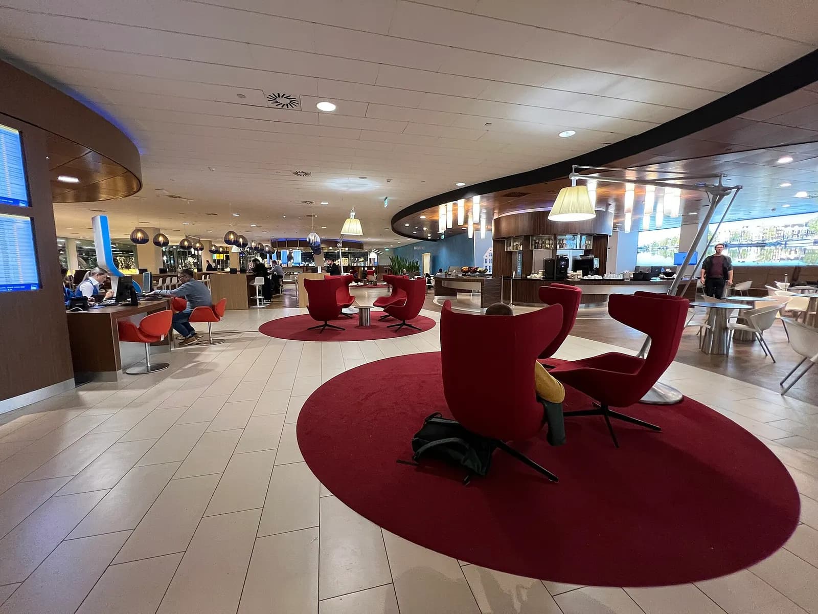 The KLM Crown Lounge at Schiphol with buffet counters, seating areas, and large windows overlooking the airfield.