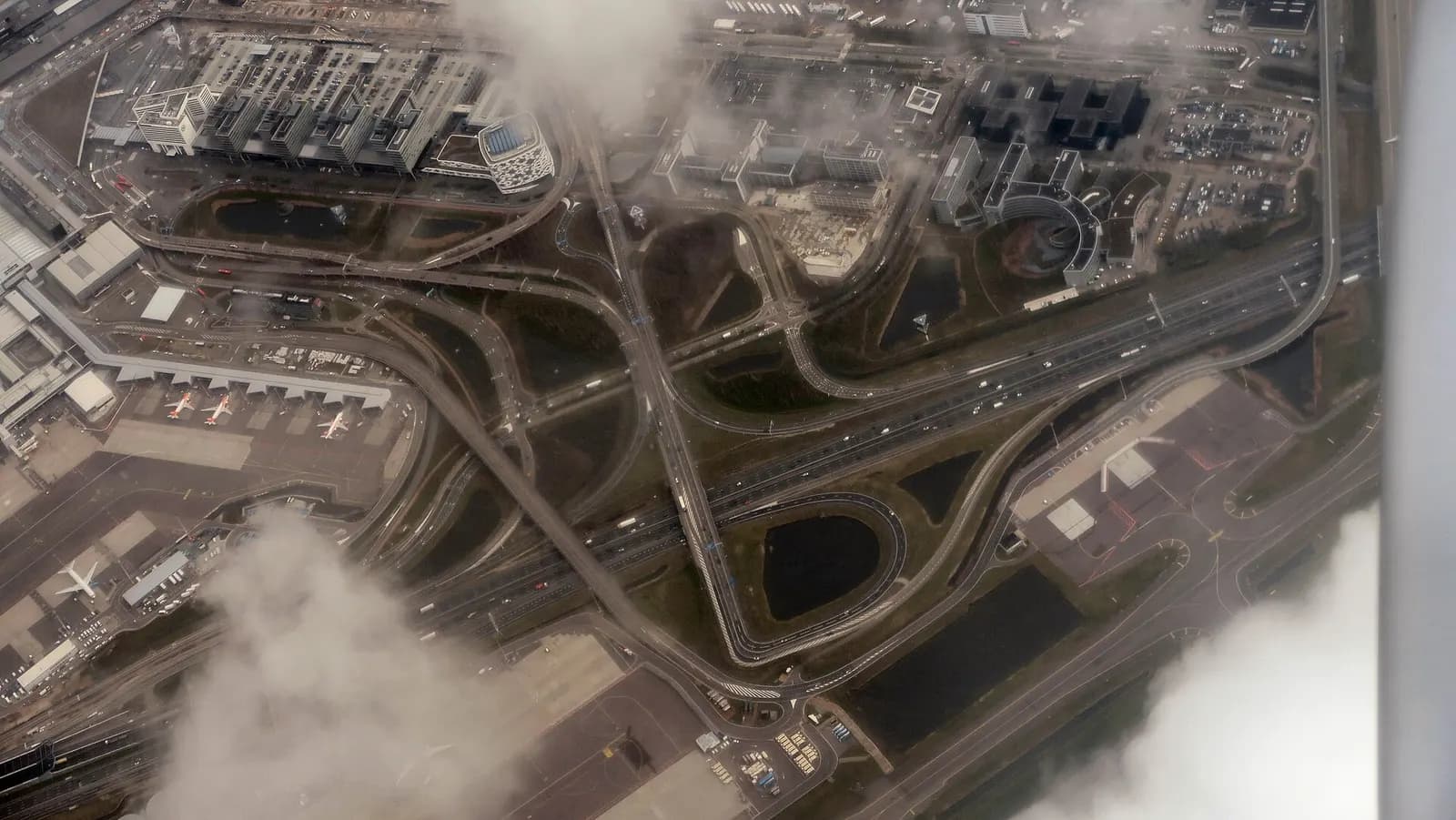 An aerial view of Schiphol showing the M-pier, terminal buildings, runways, and the A4 highway exit to the airport.