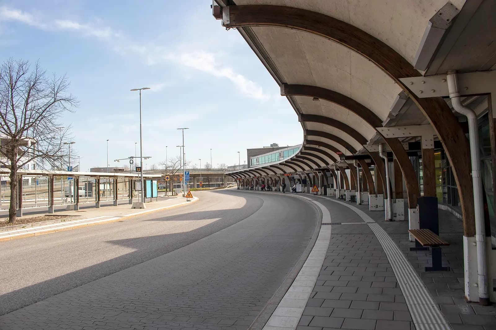 Outdoor bus stop shelter outside Terminal 4 with route signs and buses serving the airport.