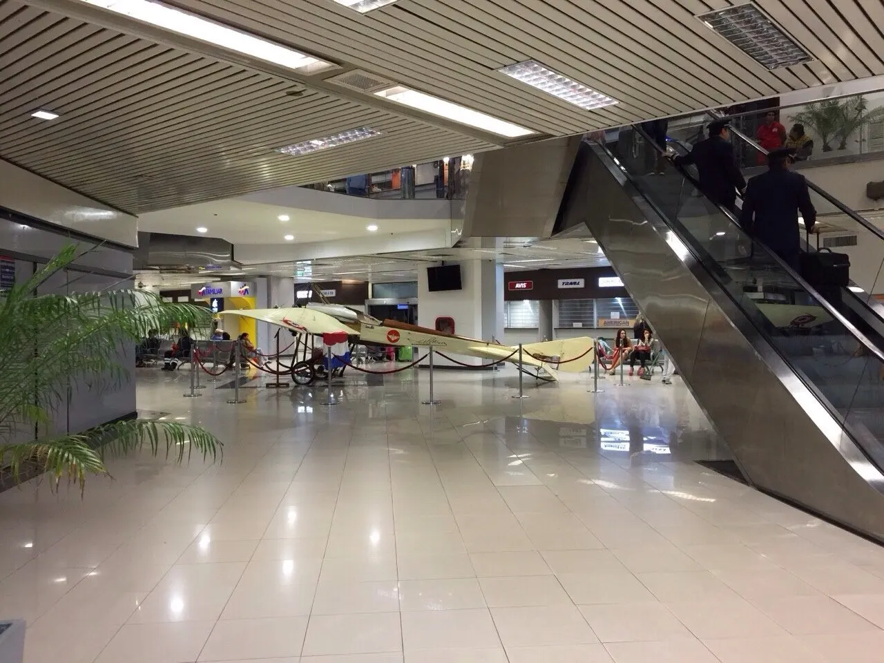 Spacious terminal lobby with shiny tile floors, an escalator, and a cream-colored vintage biplane on display in the center of the hall.