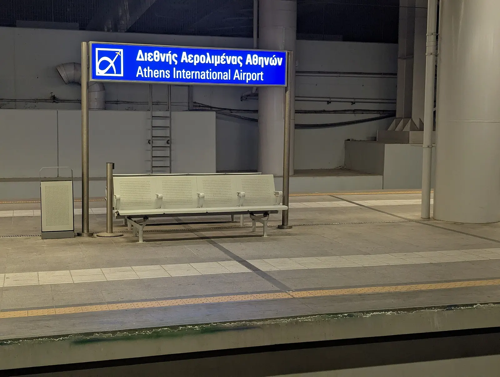 The Athens International Airport railway station platform with tracks, shelter, and signs for metro and suburban rail connections.