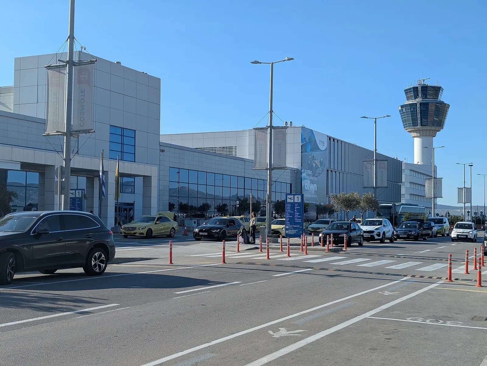 The Athens International Airport air traffic control tower and adjoining terminal structures seen from the landside on a clear morning.