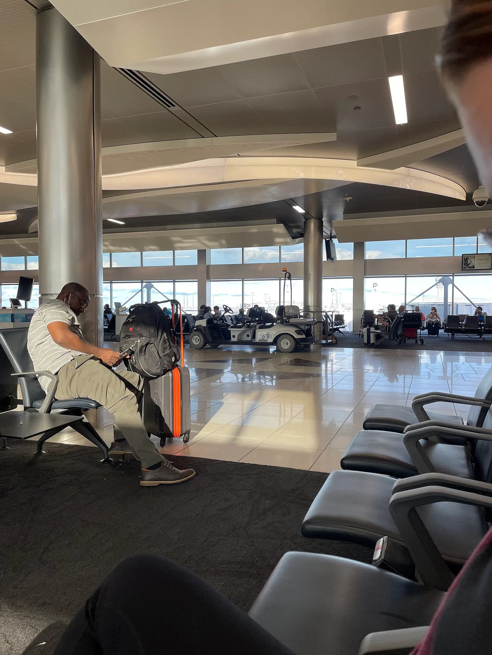 Busy interior corridor at Hartsfield-Jackson Atlanta International Airport with high ceilings, retail storefronts, directional signage, and passengers rolling luggage.