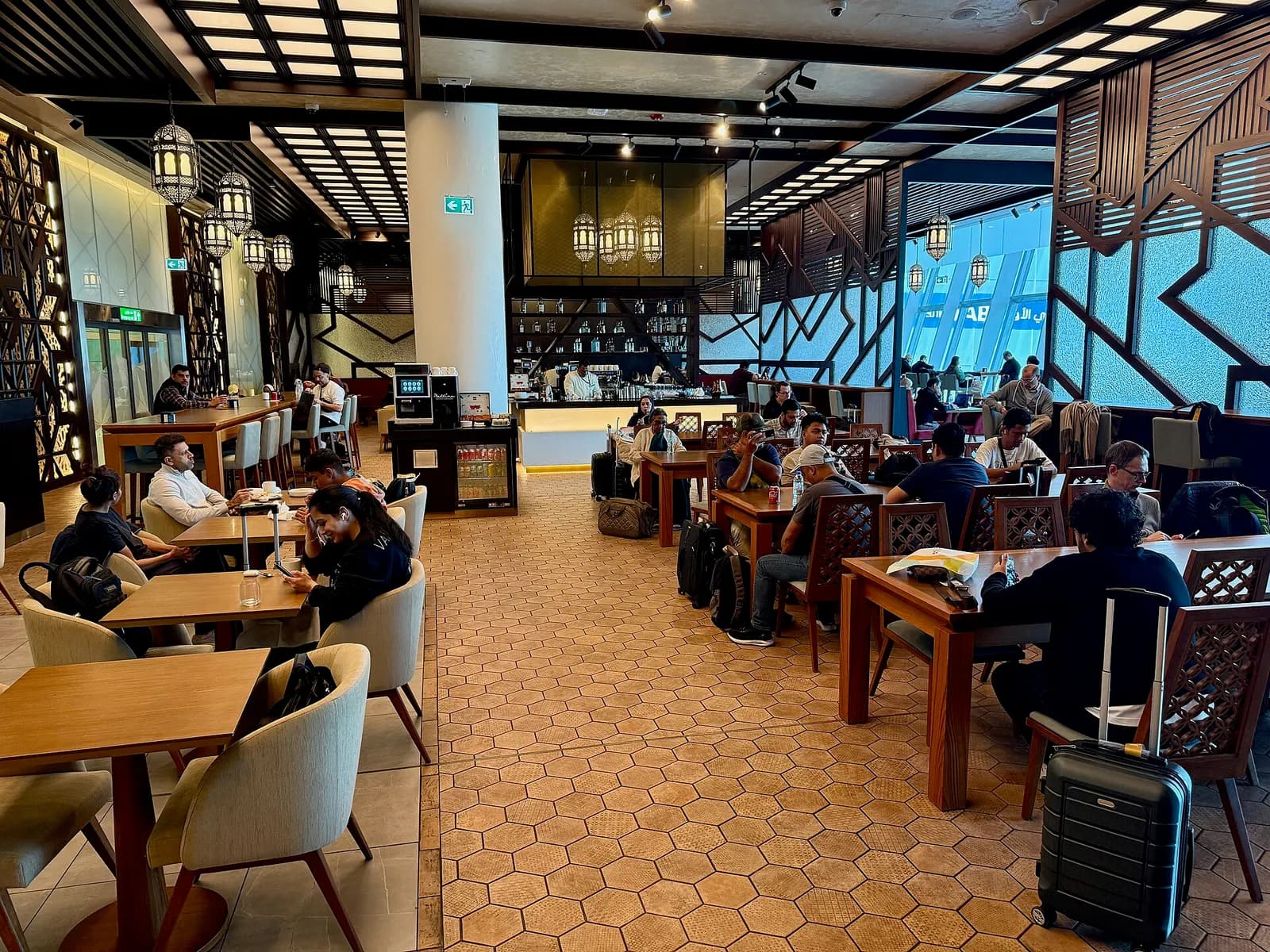 The spacious Etihad Airways Business Class Lounge with upholstered seating, tables, warm lighting, and large windows overlooking the terminal.