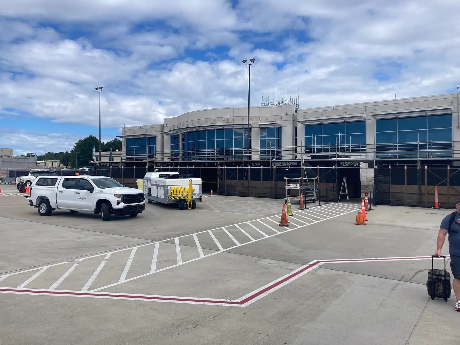 September 2023 airside view of the unfinished Asheville Regional Airport North Concourse behind scaffolding, with a ramp tug on the concrete.