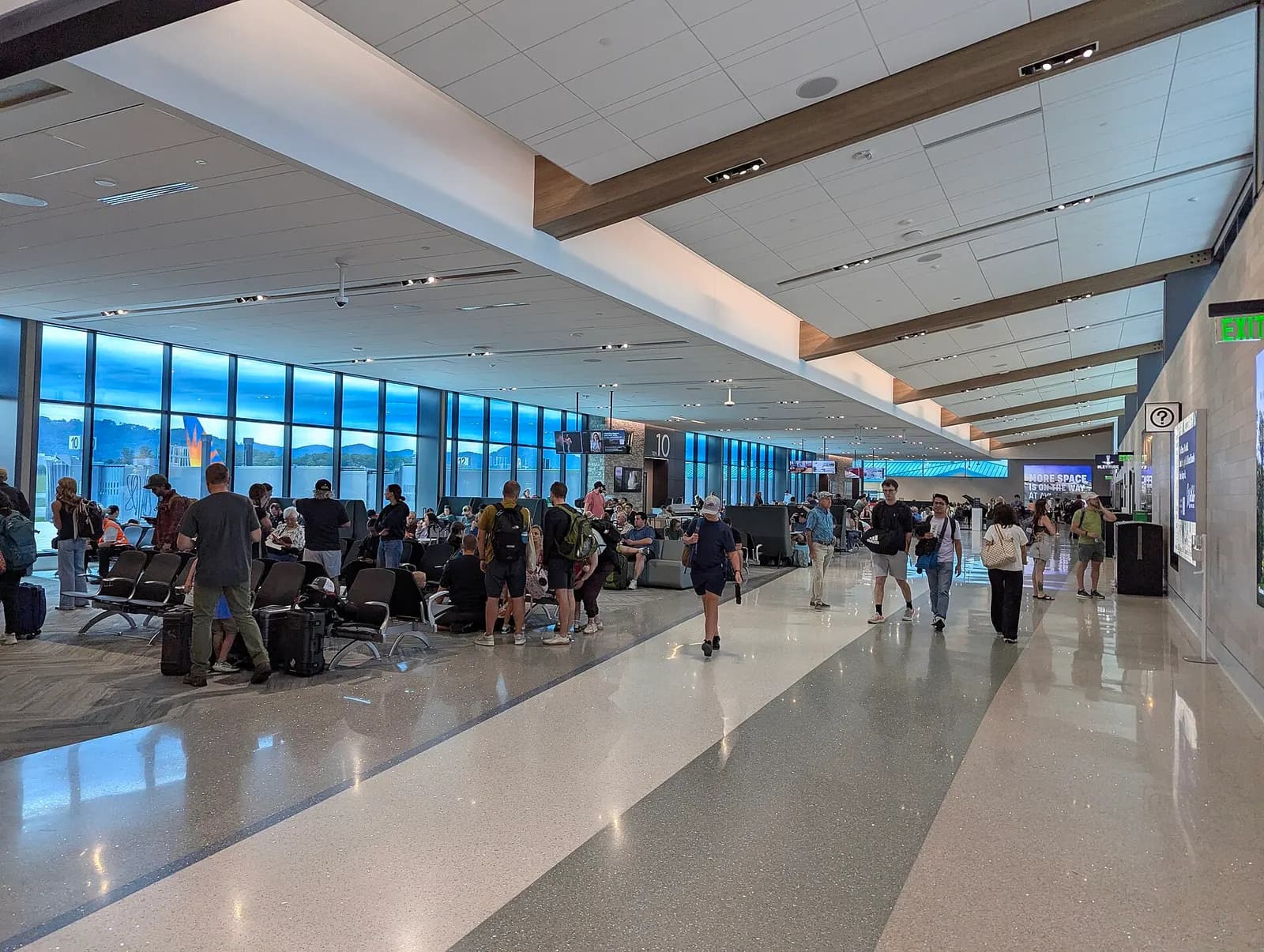 Bright North Concourse holdroom at Asheville Regional Airport in June 2026, with Gate 10 visible and travelers seated along the window wall.