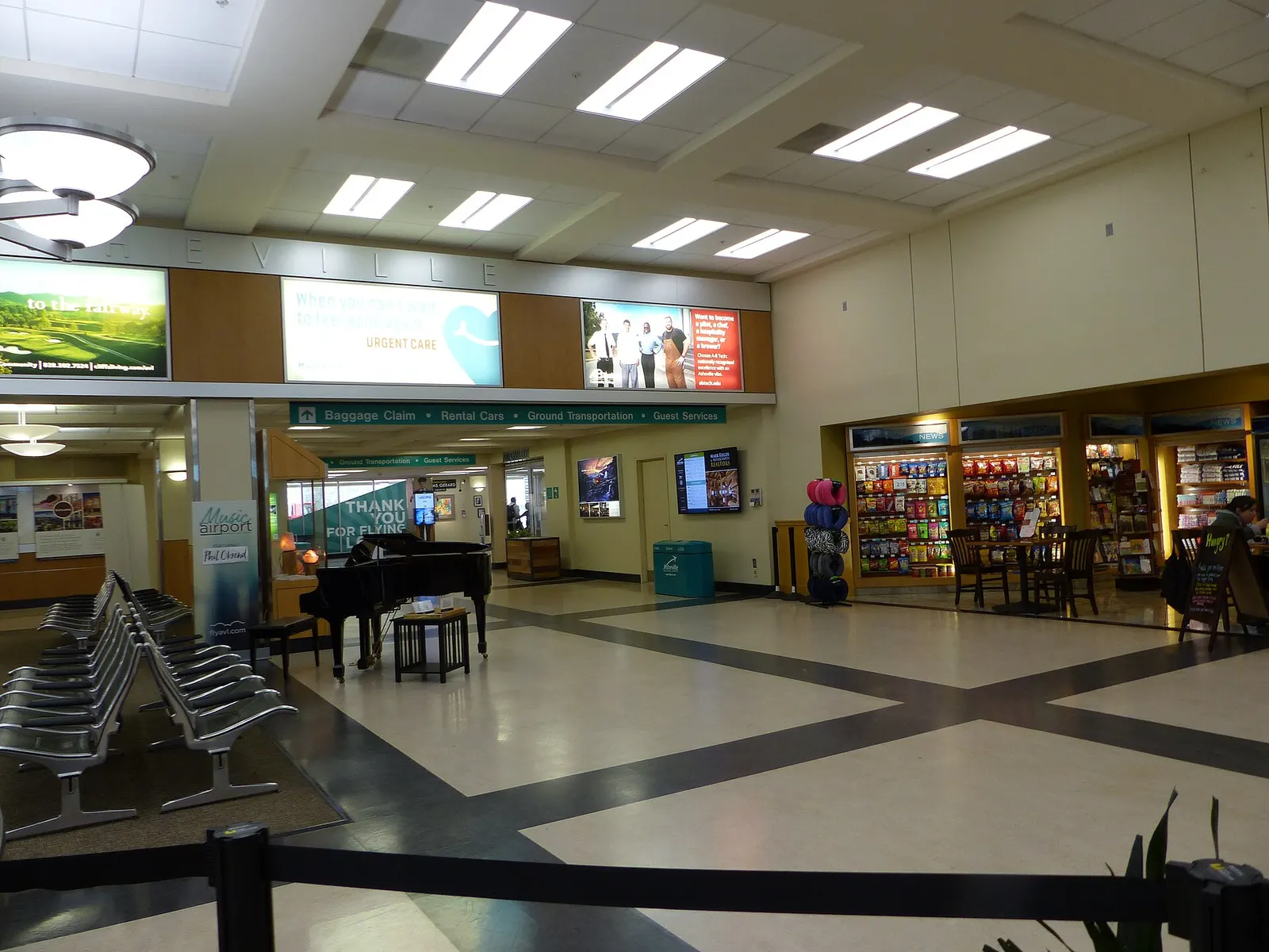 2019 Asheville Regional Airport public hall with a piano, gift racks, and signs pointing to baggage claim, rental cars, ground transportation, and guest services.