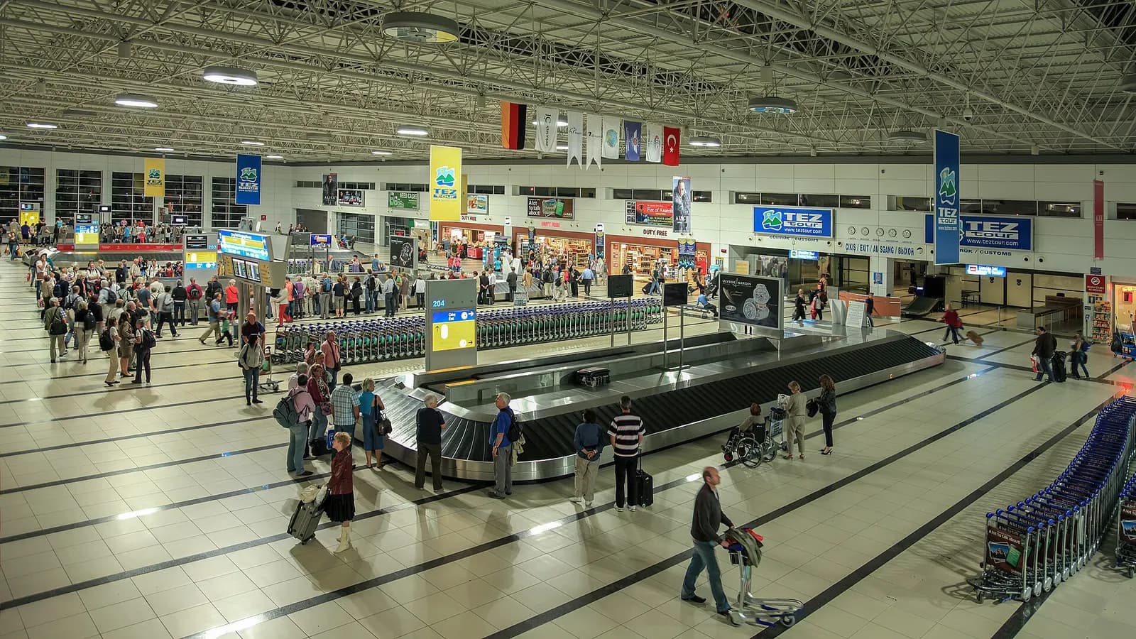 Antalya Airport baggage claim hall with multilingual exit signs and TEZ Tour banners