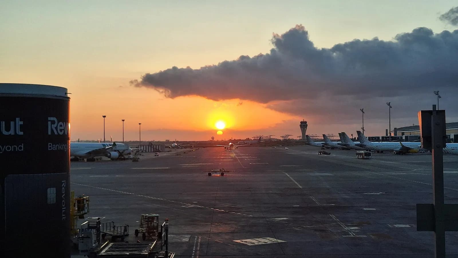 Sunrise sky over Terminal 2 at Barcelona-El Prat, with the terminal silhouette and airfield visible in early morning light.