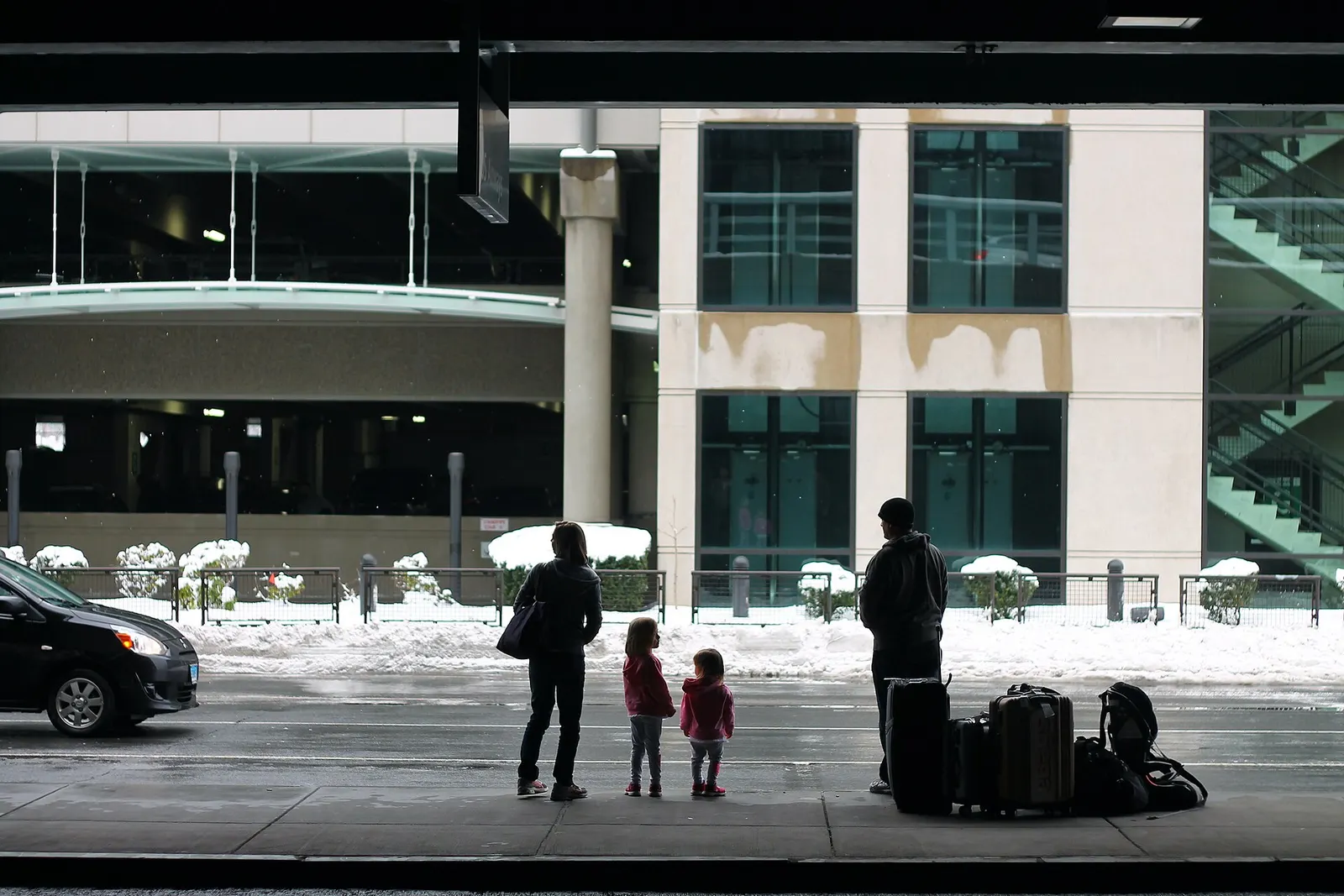 Family with luggage waiting on a snowy Bradley arrivals curb in front of the parking garage