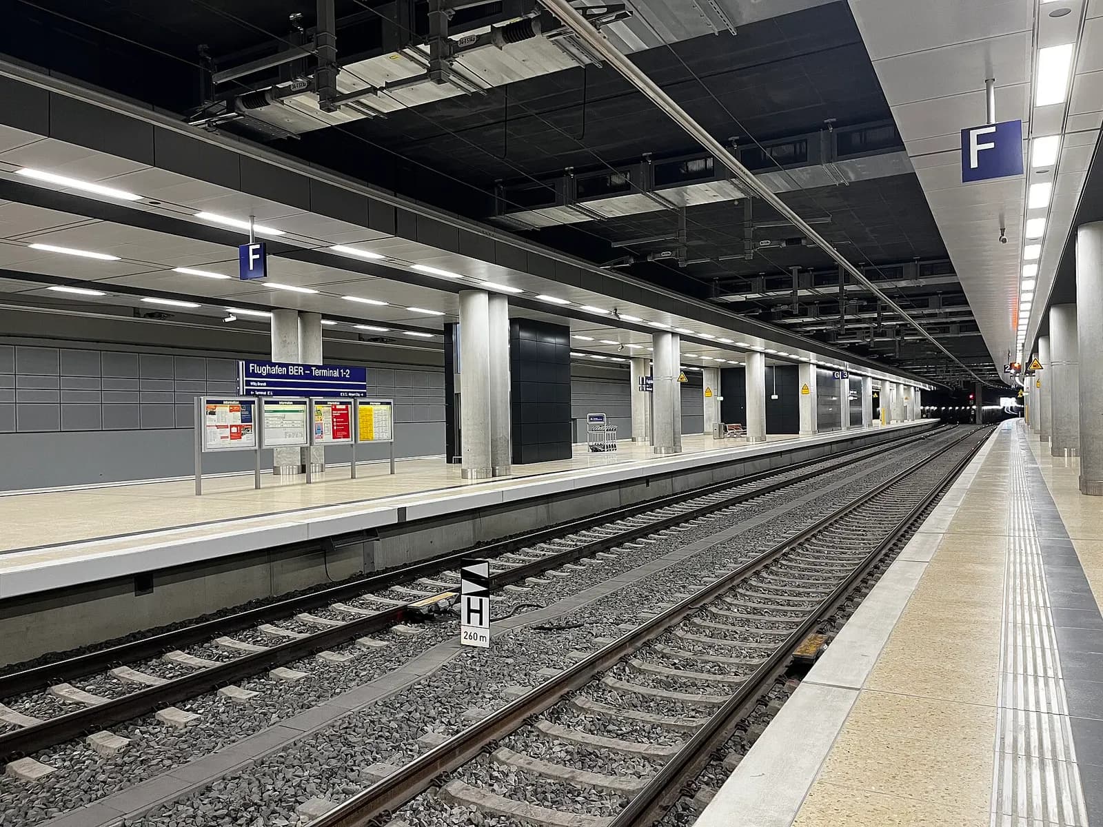 The BER Airport Terminal 1-2 station platform sits beneath the airport, with tracks, platform signage, and the station structure visible.