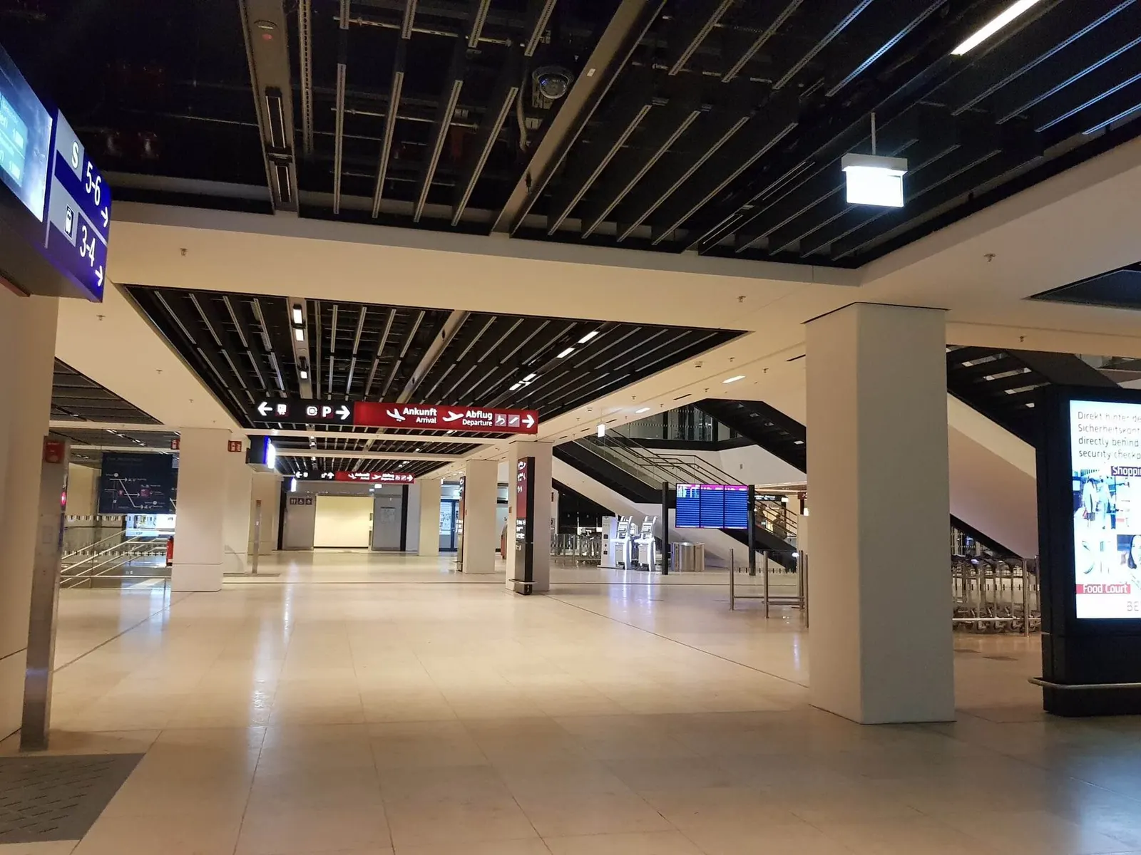 Inside Berlin Brandenburg Airport in 2023, a bright departures hall shows seating areas, signage, and travelers moving through the terminal.
