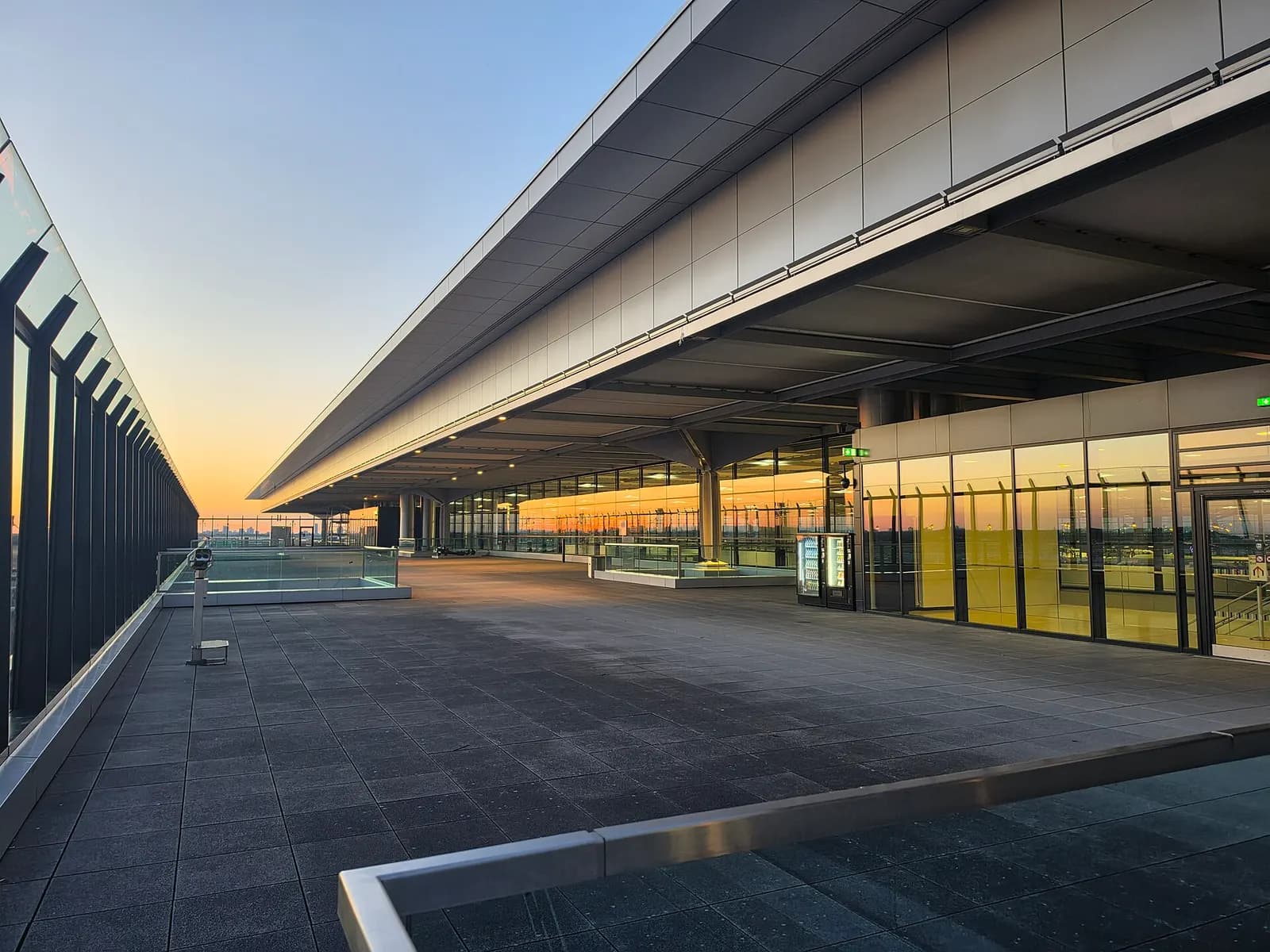 The public observation deck at Berlin Brandenburg Airport has safety railings and overlooks the airfield, taxiways, and terminal rooftops.