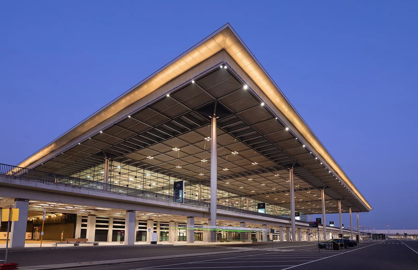 Berlin Brandenburg Airport Terminal 1 is lit up at night, with warm light glowing through the terminal's glass and concrete exterior.