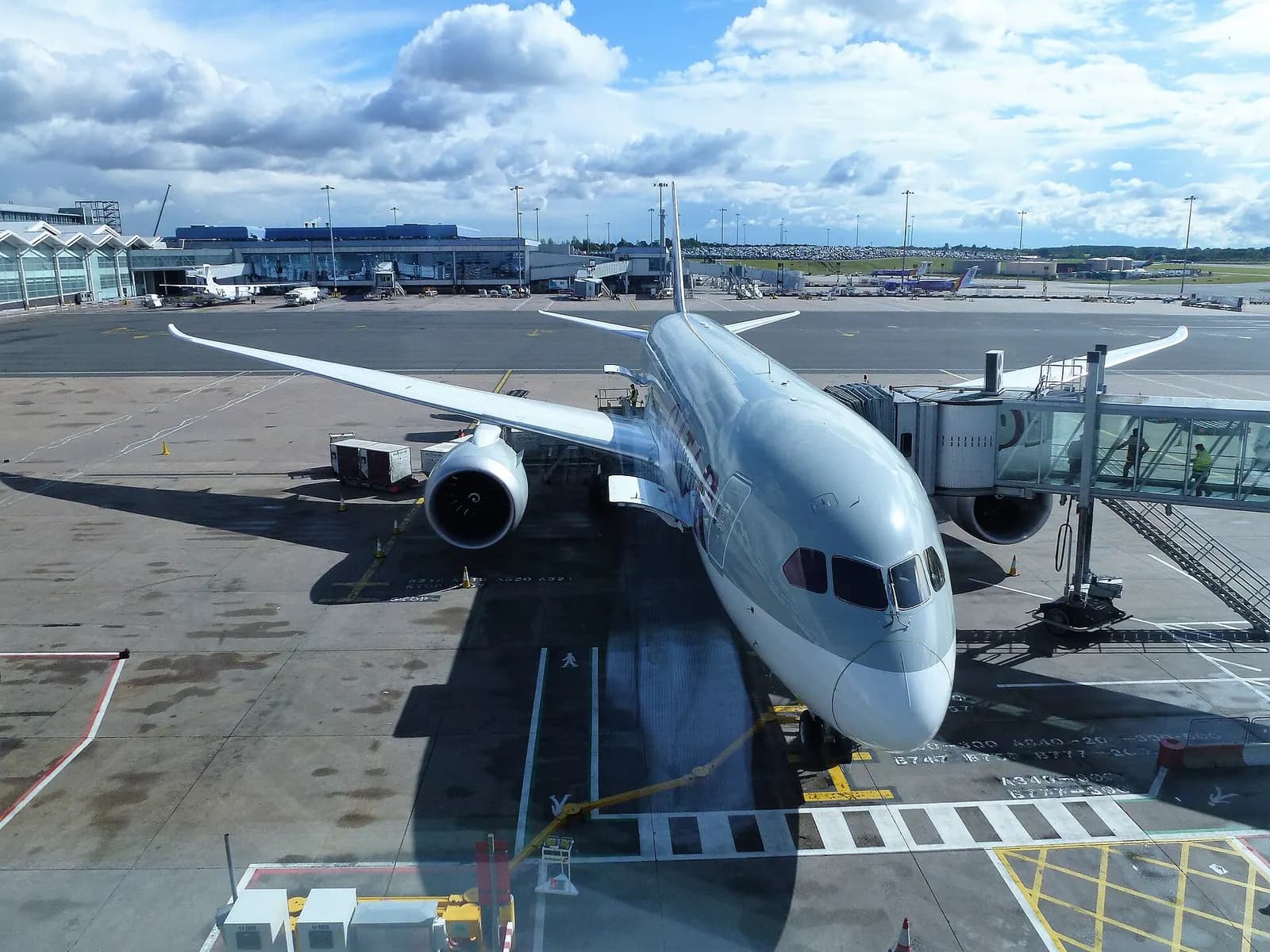 Passengers boarding a Qatar Airways aircraft at a Birmingham Airport gate via stairs on the tarmac.