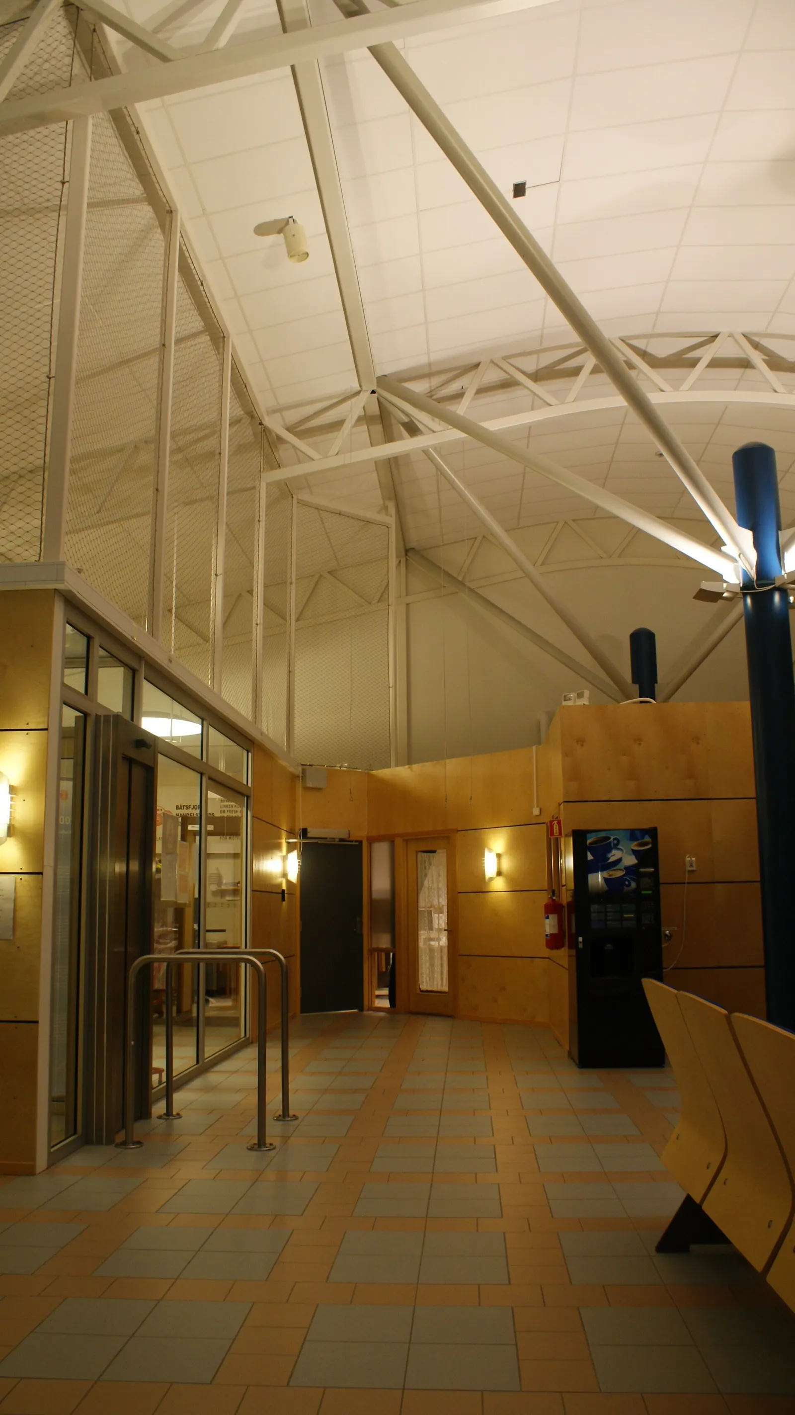Airside departure hall inside Båtsfjord Airport’s single passenger terminal, with seating and windows overlooking the apron.