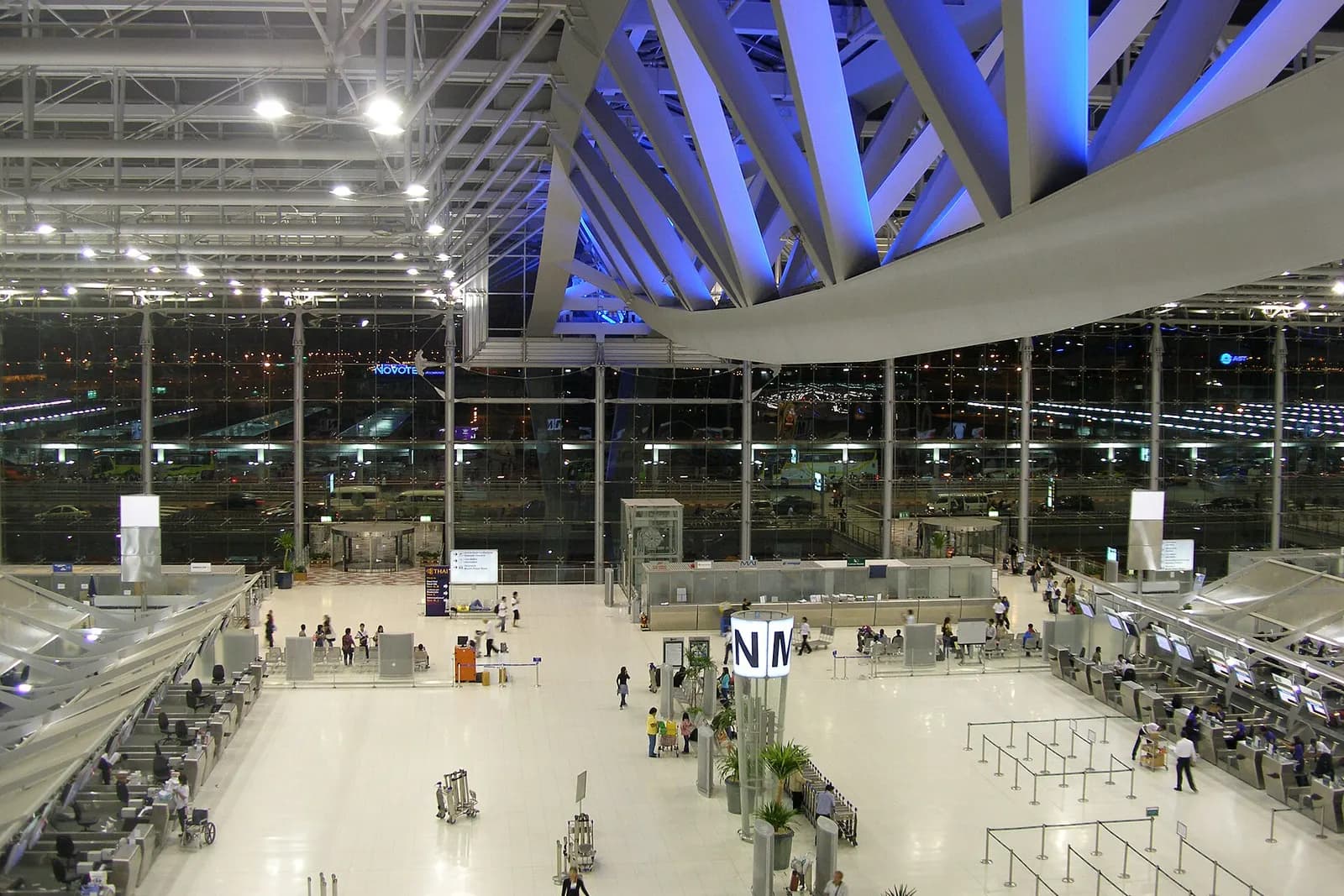The vast main departure hall of Suvarnabhumi Airport with its sweeping curved roof, glass walls, and travelers moving through the open concourse.