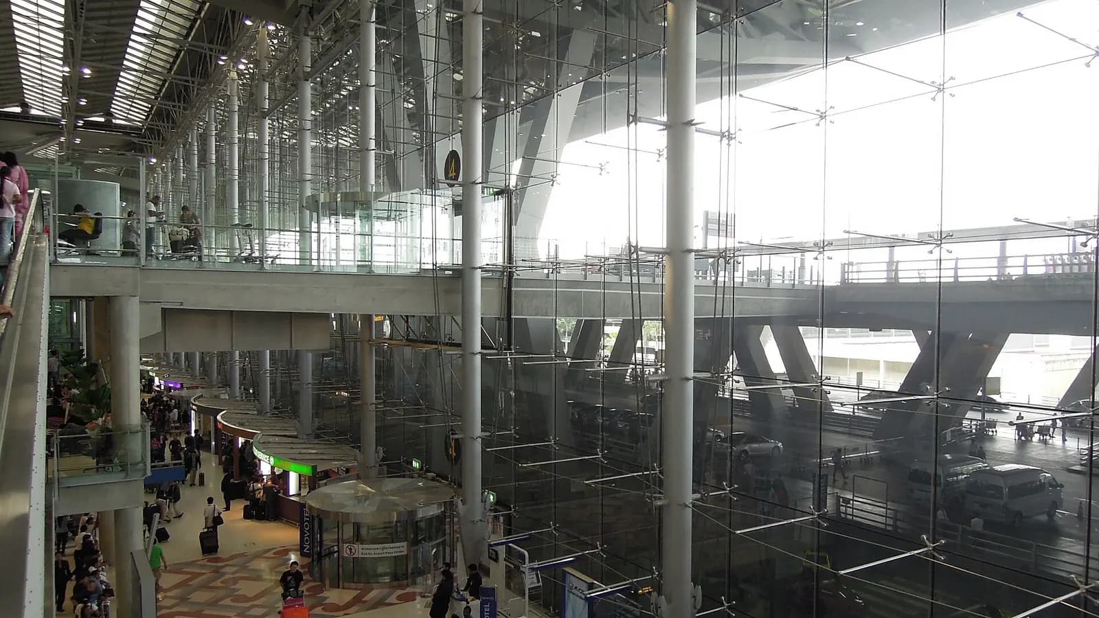 The arrivals level concourse with high ceilings, directional signs, and passengers walking past shops and service counters.