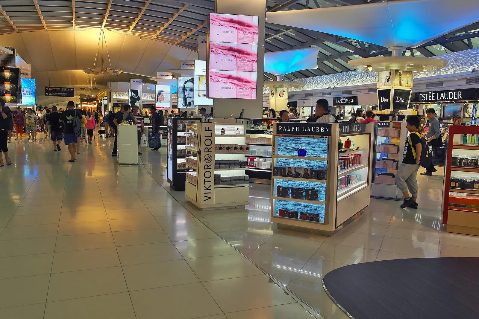 Duty-free shops and retail storefronts lining a wide, well-lit concourse corridor in the departures area.