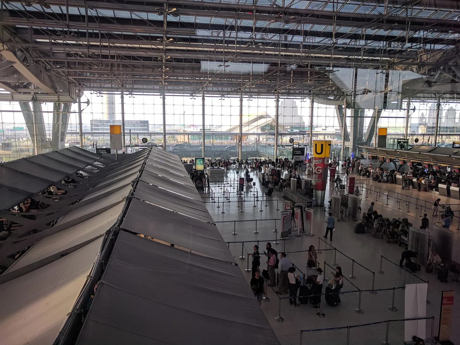 Rows of airline check-in counters in the international departures area, viewed from an upper-level balcony with travelers and luggage below.