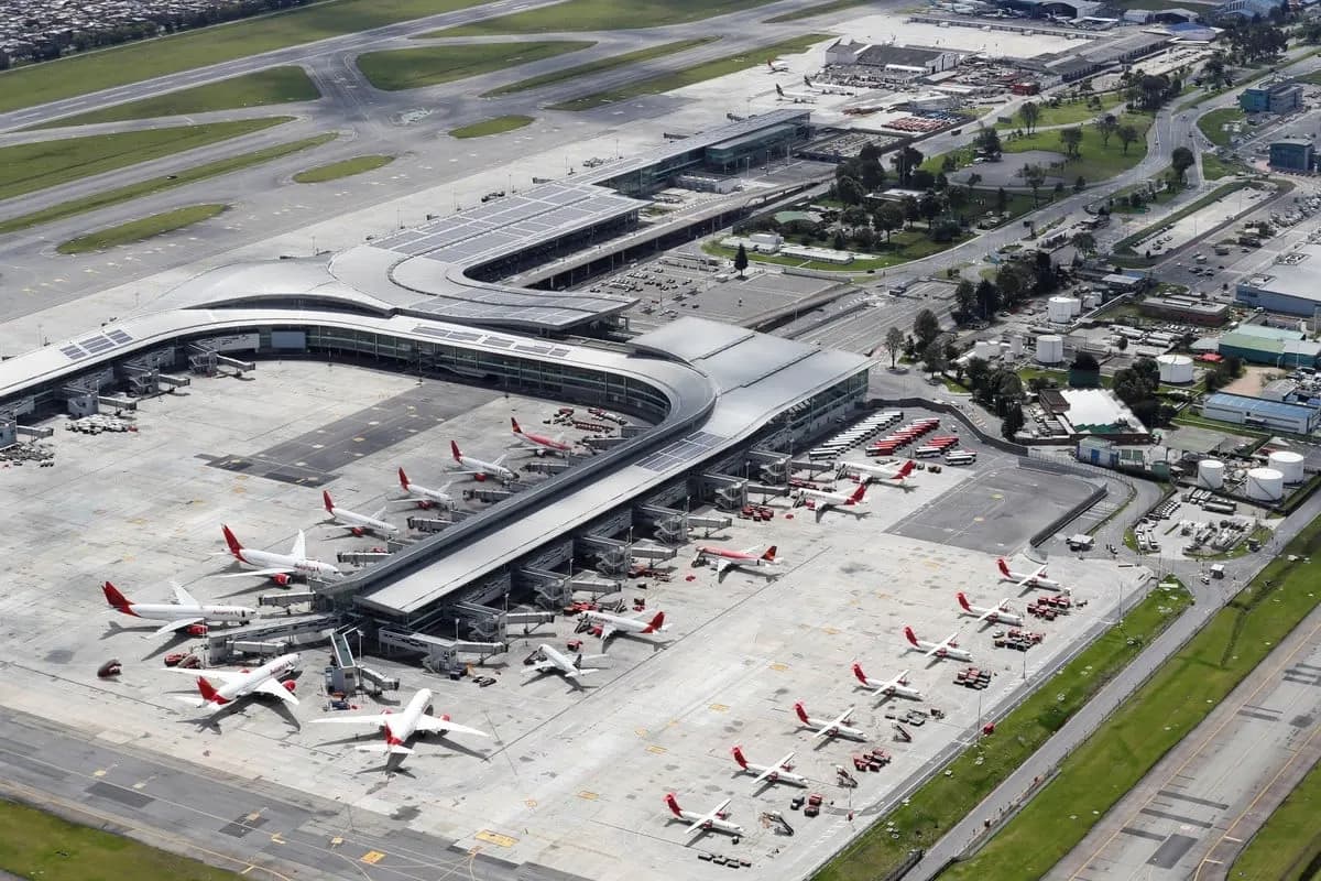 An aerial view of the curved El Dorado terminal building surrounded by parked airliners, taxiways, and runways under a clear sky.