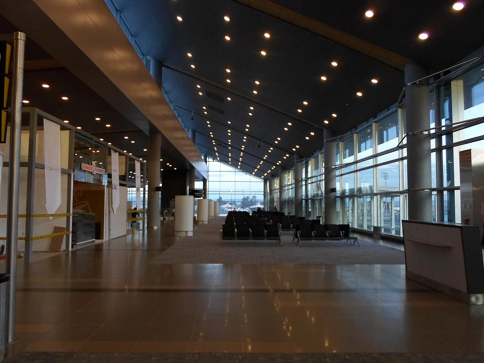 Empty black airport seating faces tall windows overlooking the airfield in the domestic terminal's polished, high-ceilinged waiting area.