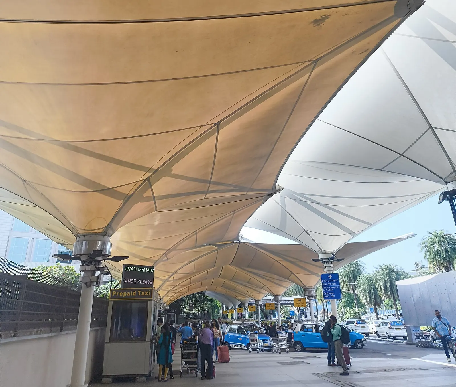 The sweeping white tensile fabric roof canopy arches over the roadway and entrance area outside the airport terminal.