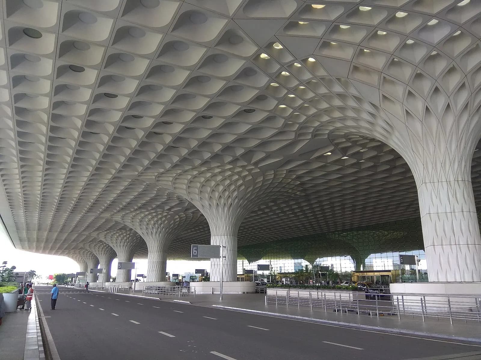 Passengers gather in a departure concourse beneath overhead flight-information displays, directional signs, and a high ceiling.