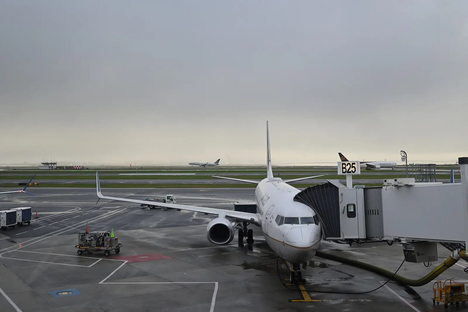A United Boeing 737 waits at gate B25 while another United plane lands and a UPS cargo jet taxis on the ramp.