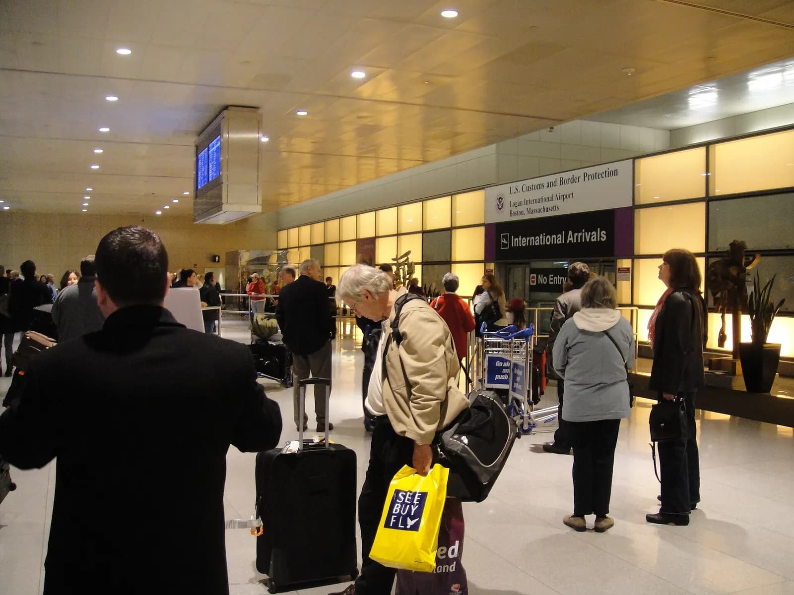 The wide lower-level international arrivals hall in Terminal E with tiled floors, support columns, and BOS airport signage.