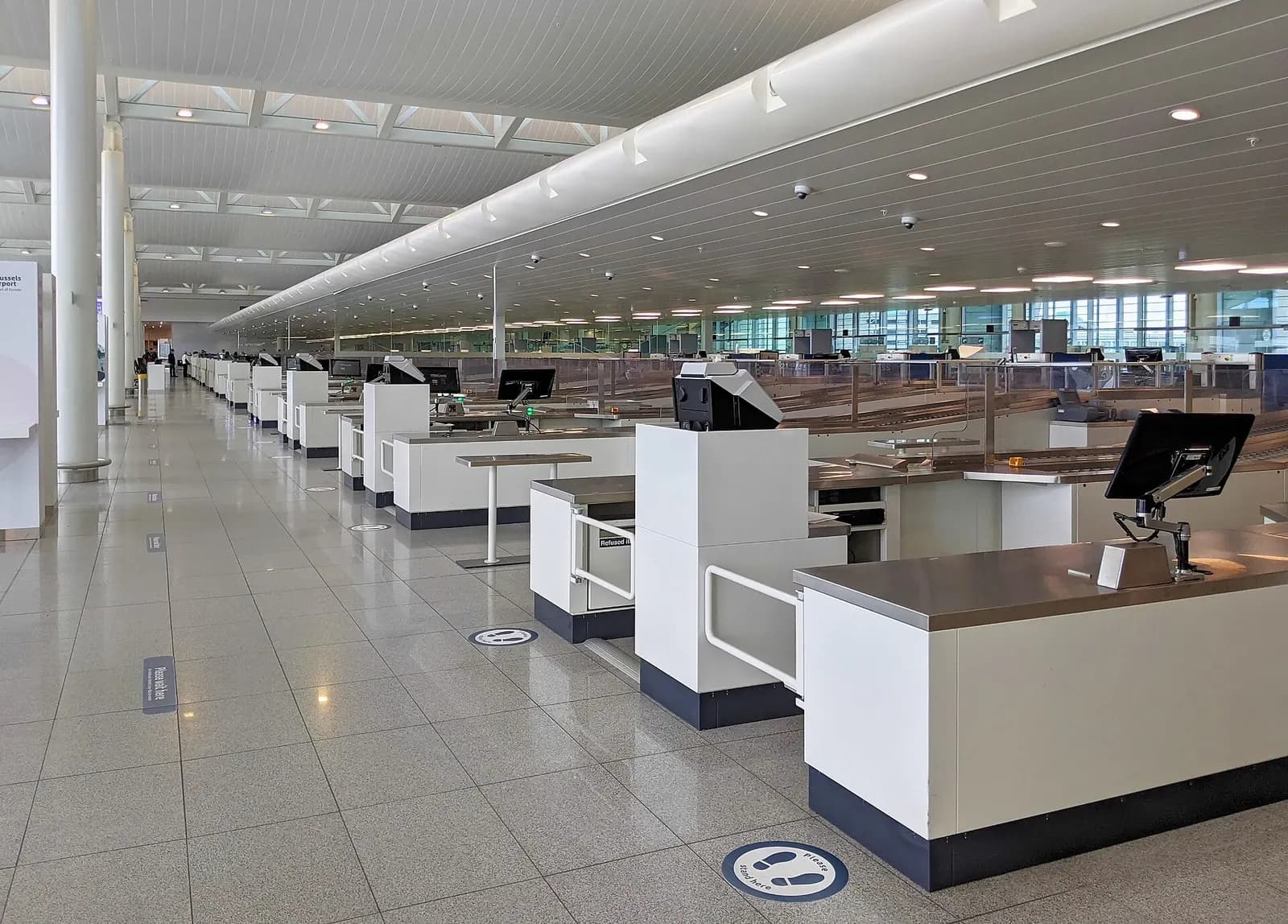 A wide security screening hall at Brussels Airport with multiple lanes, conveyor belts, and x-ray equipment.