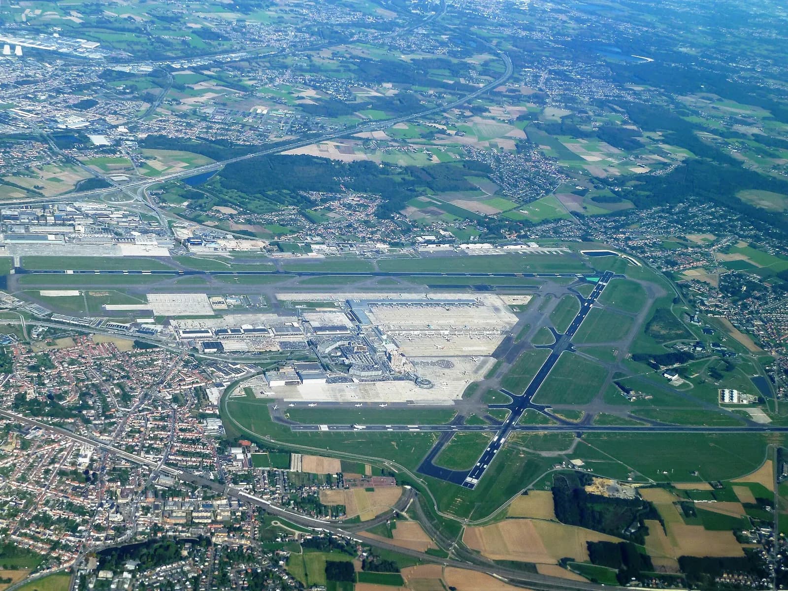 An aerial view of Brussels Airport showing parallel runways, terminal buildings, aprons, and surrounding countryside.
