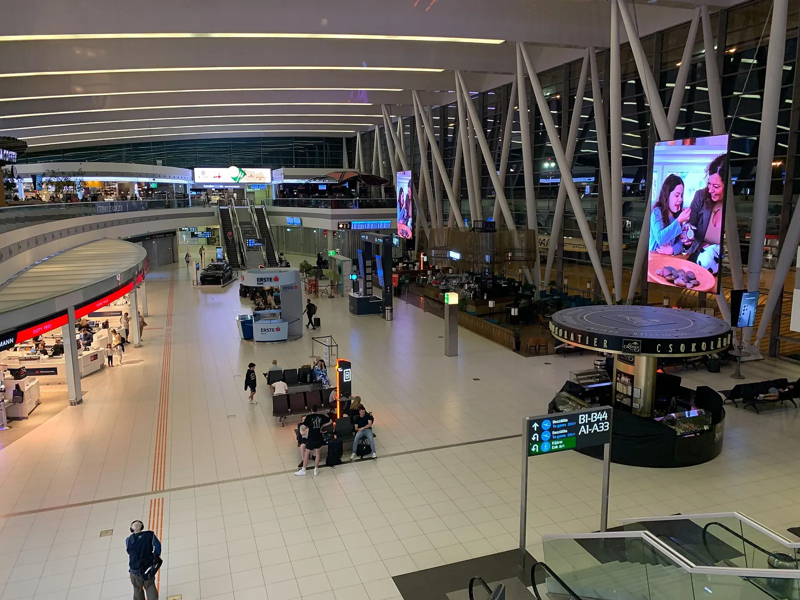 The bright SkyCourt concourse inside Terminal 2, with high ceilings, shops, and passengers walking through the central linking hall.