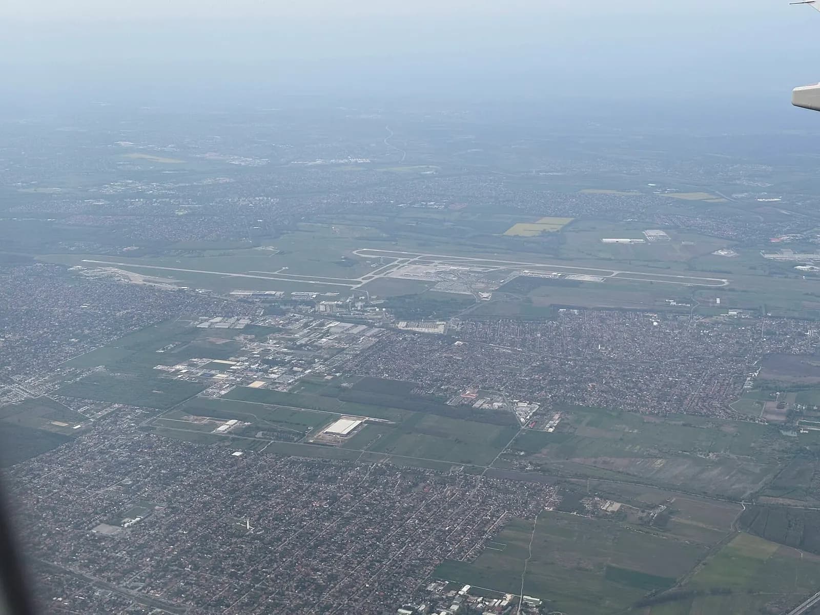An aerial photograph of Budapest Ferenc Liszt International Airport taken from a passenger plane, showing runways, taxiways, and the terminal complex.