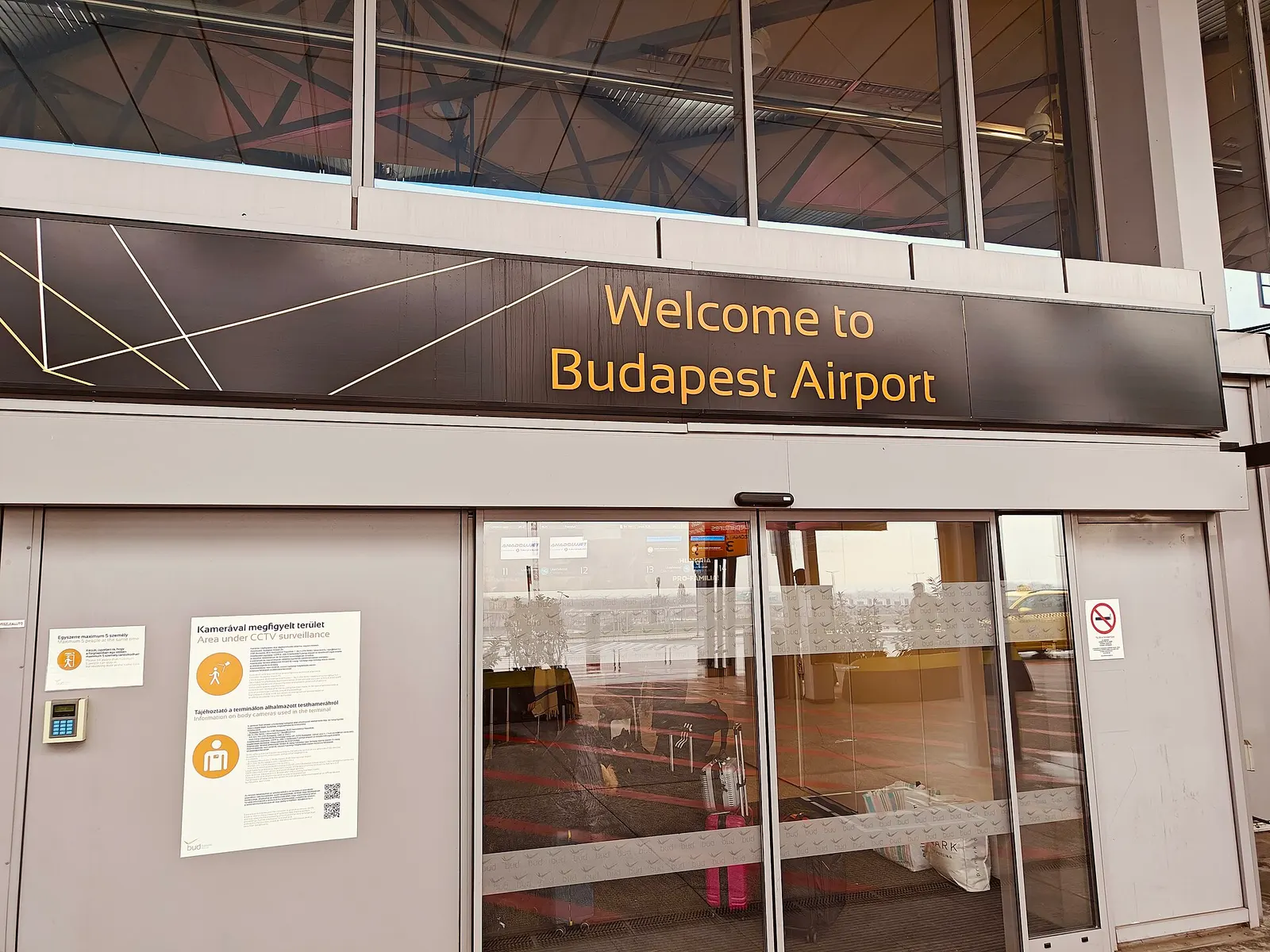 The glass-fronted departures entrance of Budapest Ferenc Liszt International Airport with terminal signage and travelers approaching the building.