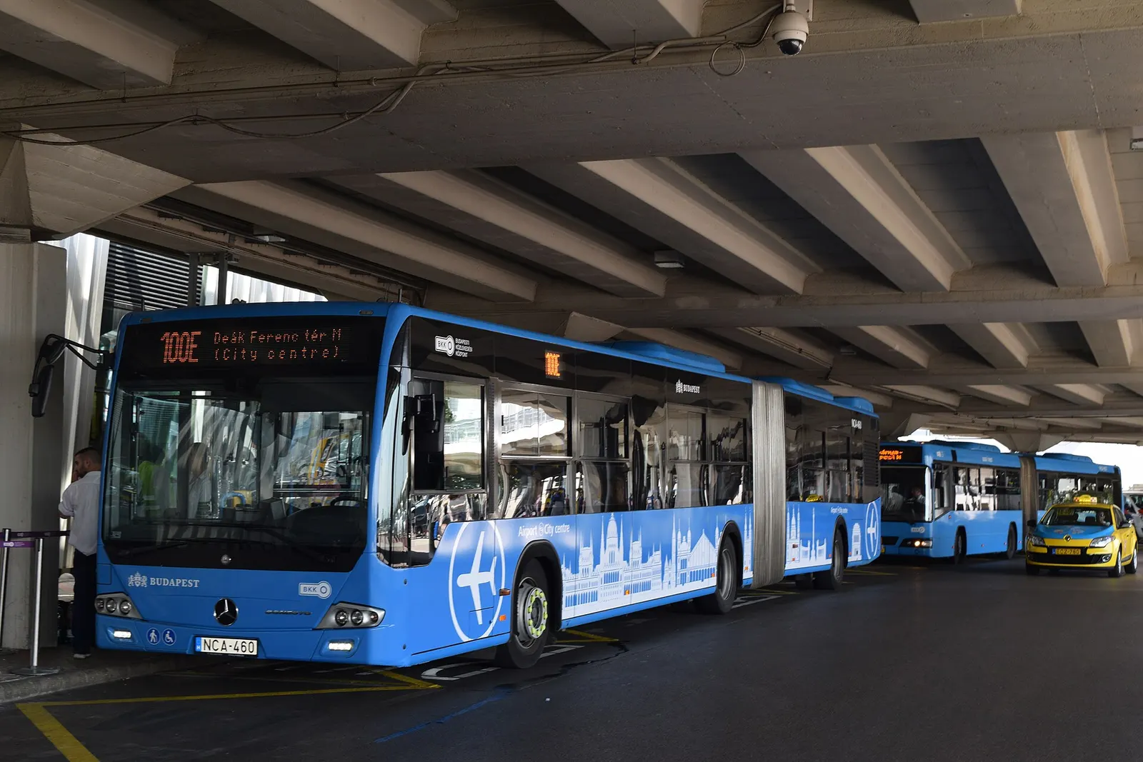 Two public buses parked outside the airport: route 100E to central Budapest and route 200E to Kőbánya-Kispest metro station.