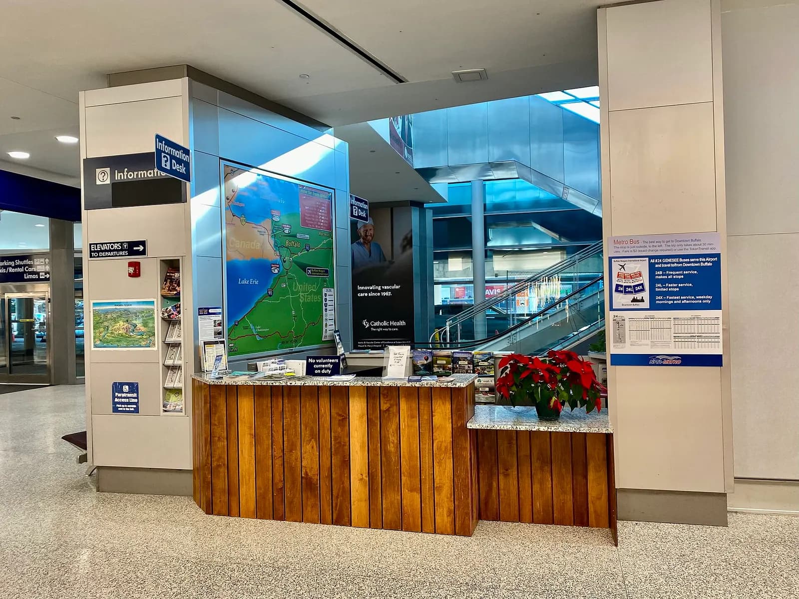 Visit Buffalo Niagara tourist desk on the arrivals level opposite baggage claim, with a regional map, Metro Bus 24 poster, and elevator-to-departures sign.