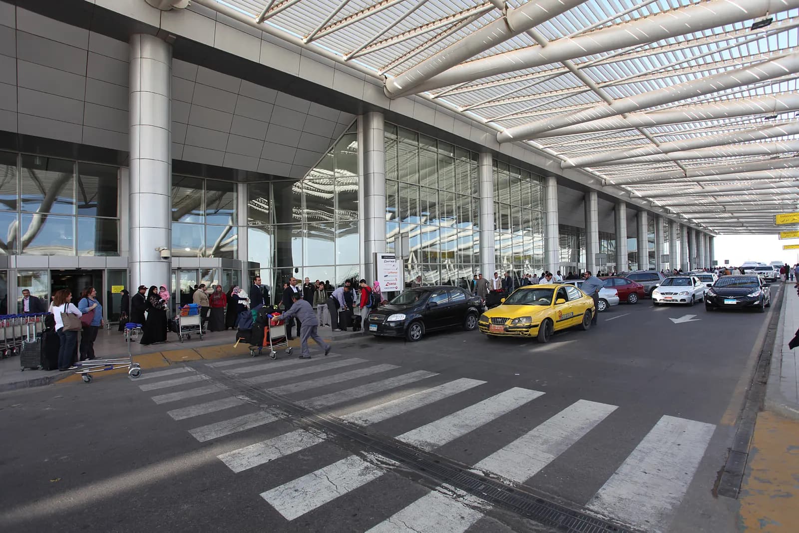 Wide view of the modern glass-and-steel facade of Terminal 3 at Cairo International Airport under a clear sky.