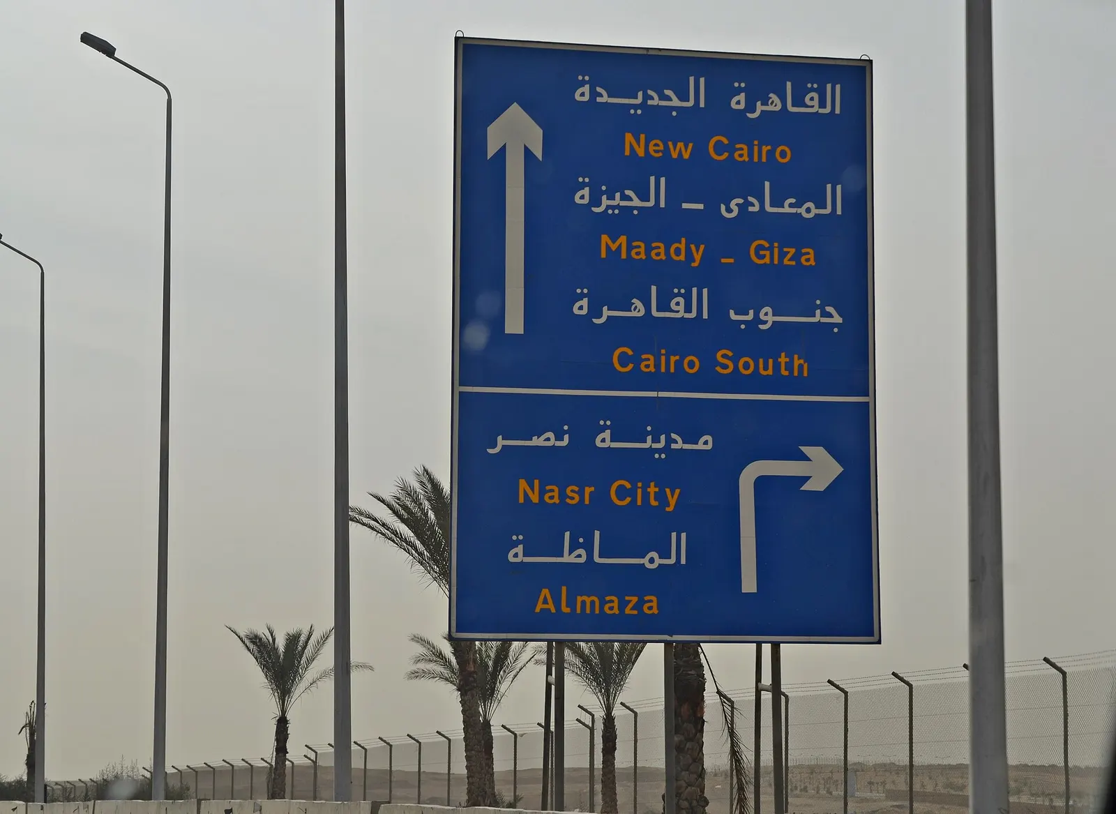 Bilingual Arabic and English directional signs hanging in a Cairo International Airport terminal corridor.