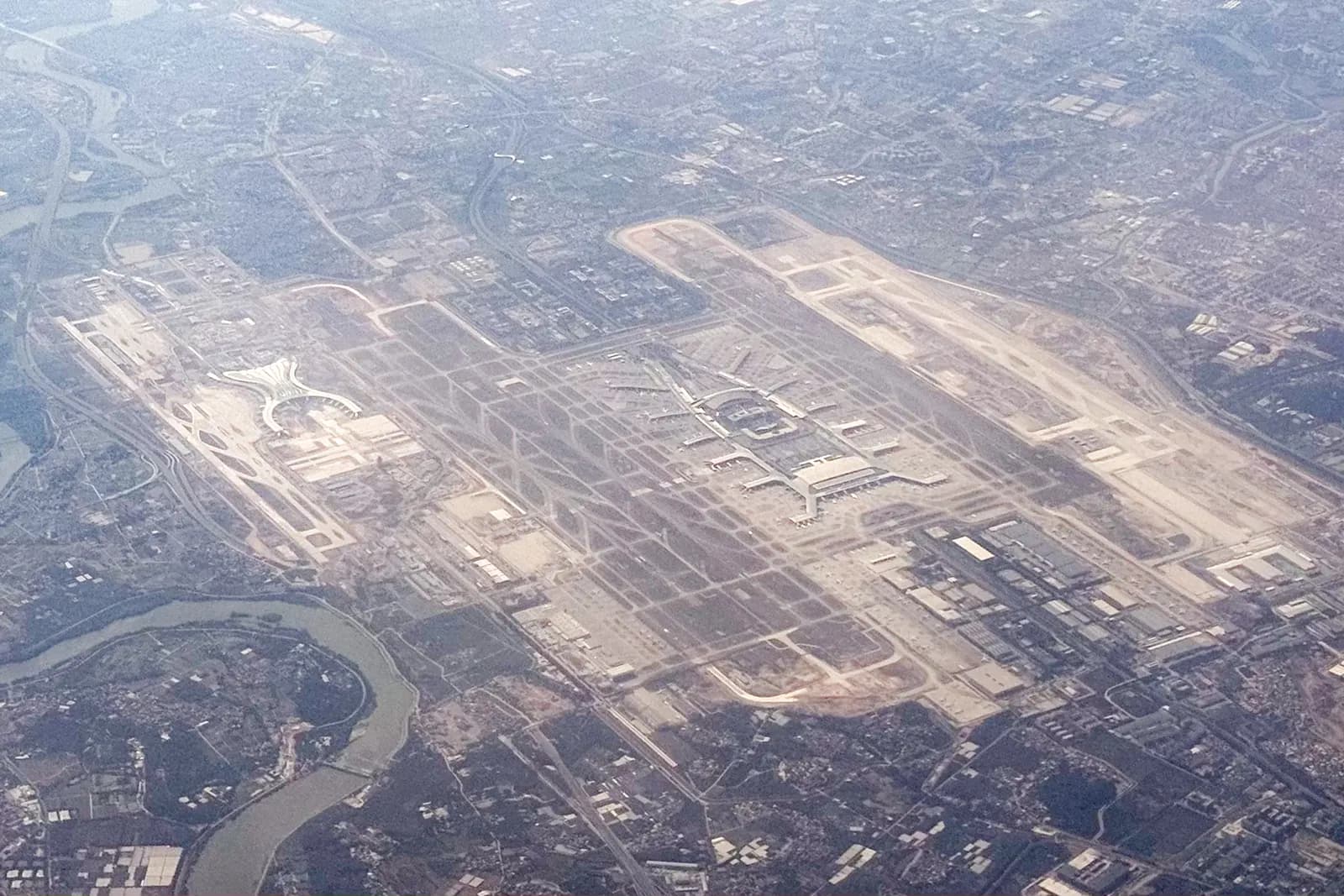An aerial photograph showing Guangzhou Baiyun International Airport's parallel terminal buildings, runways, taxiways, and surrounding countryside.