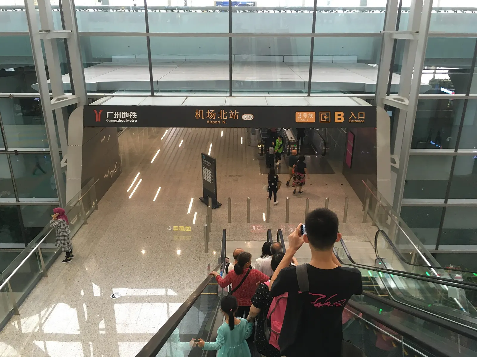 An indoor pedestrian corridor in Terminal 2 with overhead signs pointing toward Metro Airport North Station Entrance B.
