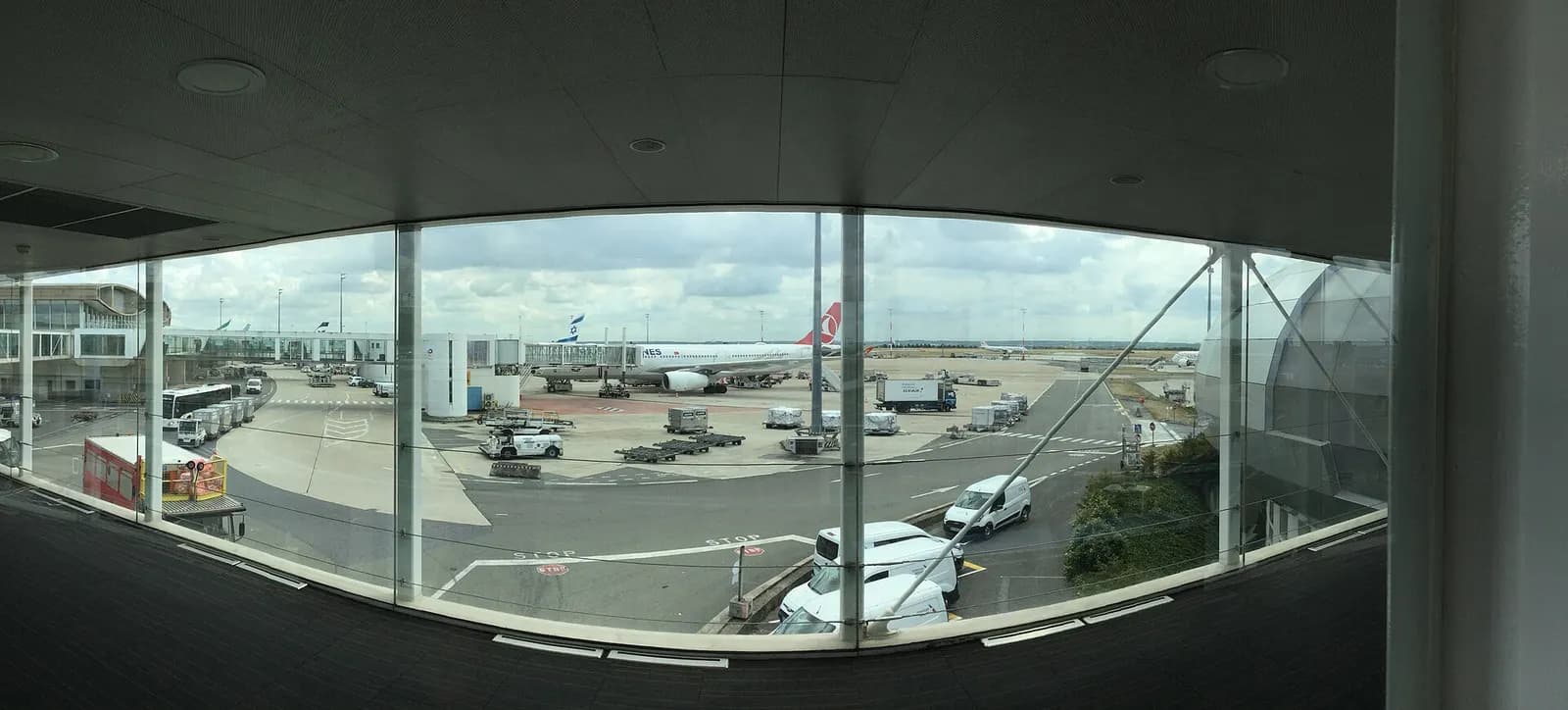 A wide panoramic view from inside Terminal 2A's walkway windows overlooking the apron, jet bridges, and parked aircraft.