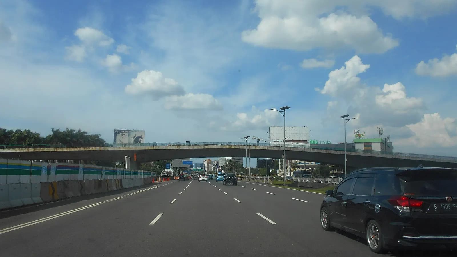 Multi-lane elevated airport access highway leading toward Soekarno-Hatta, with guardrails, overhead signs, and open sky above the roadway.